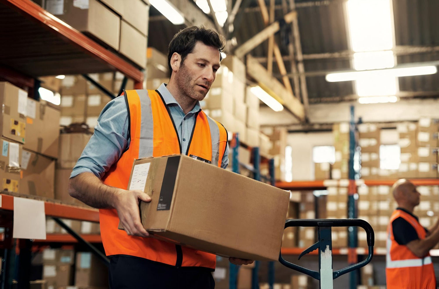 Alt text: Warehouse worker handling a cardboard shipping box in a logistics warehouse.Â