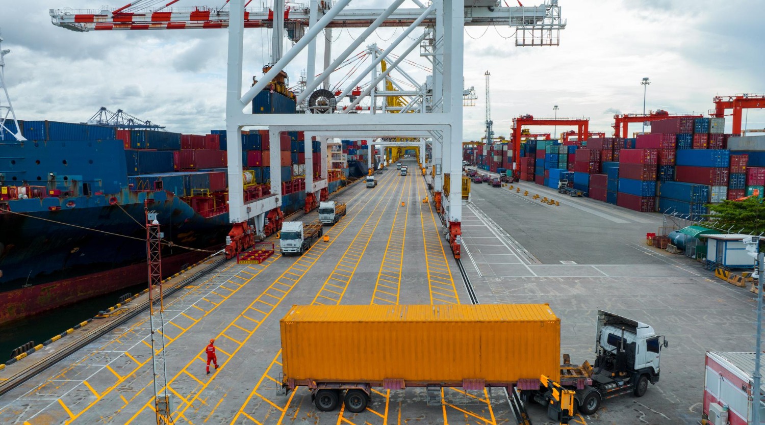 Alt text: Container ship and cargo containers at a busy international port terminal.