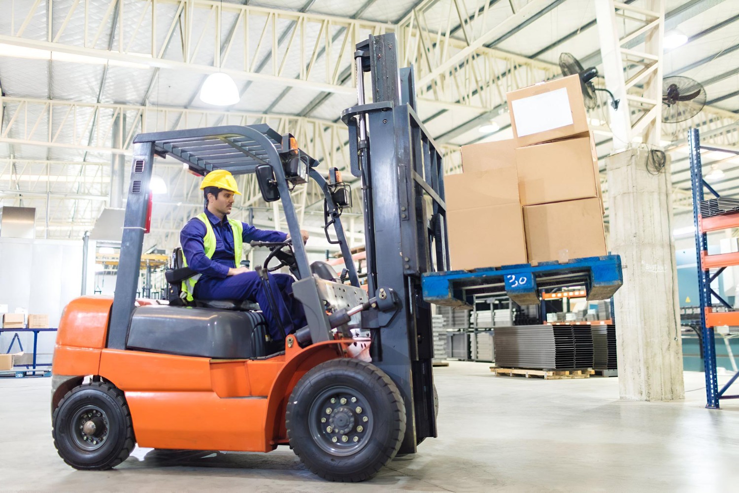 Alt text: Forklift operator transporting a pallet of cardboard boxes inside a warehouse.