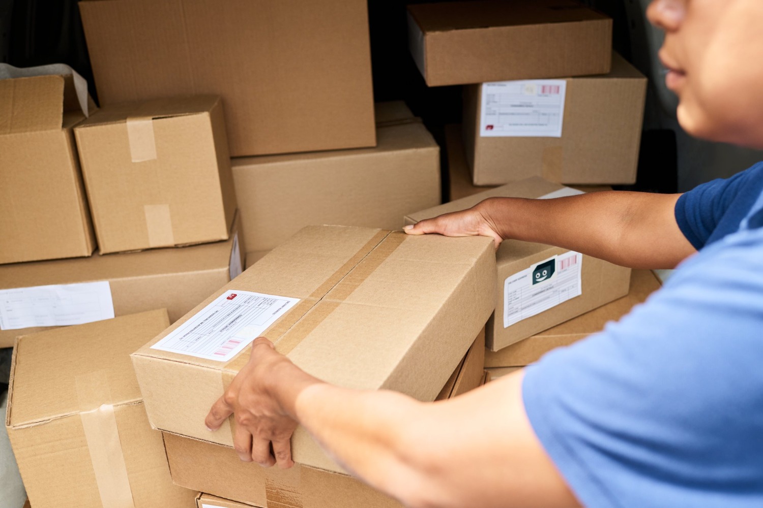 Alt text: A worker handling a cardboard parcel among stacked shipping boxes in a warehouse.