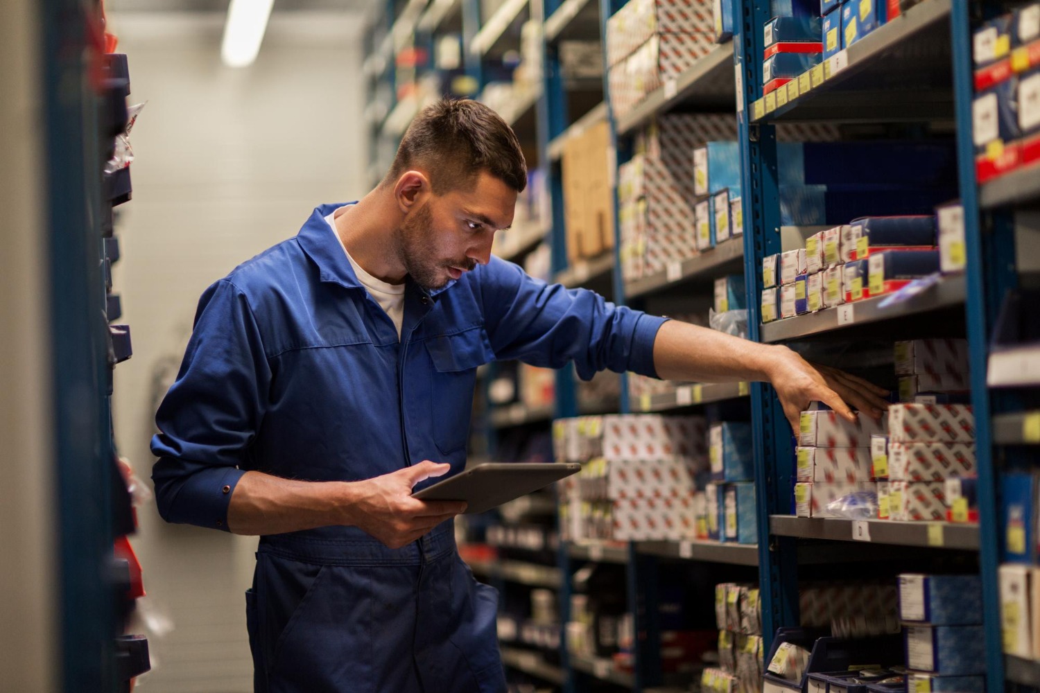 Alt text: Warehouse worker using a tablet to manage inventory in a warehouse aisle.