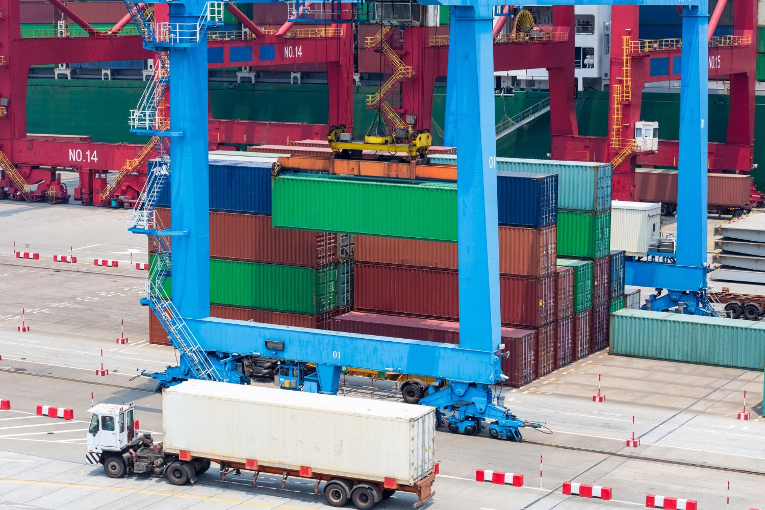 Alt text: Cargo containers being loaded at a busy port terminal using a large gantry crane, with a container truck in the foreground.