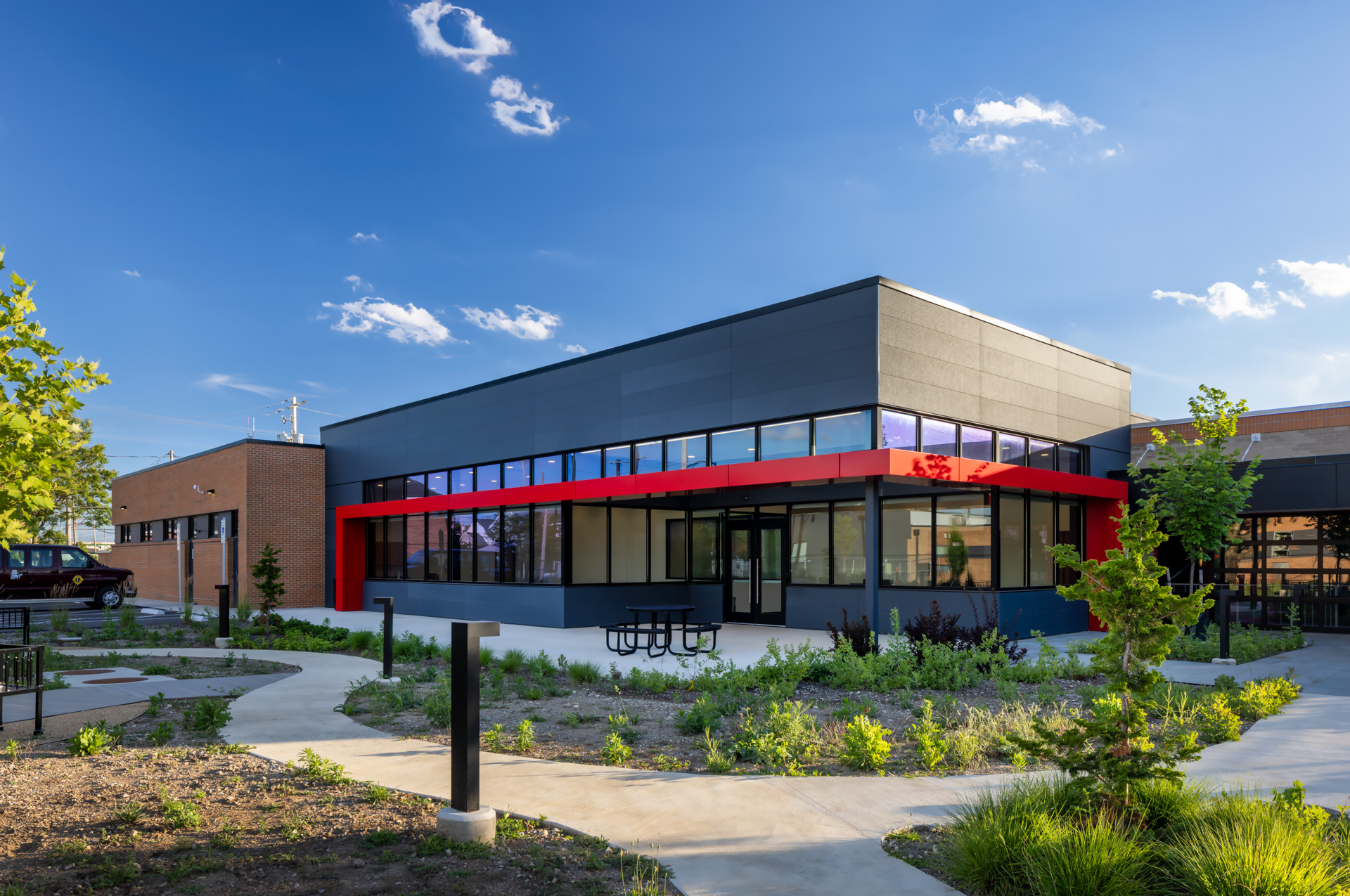 Exterior of the Pilot Dogs Puppy Palace with dark metal panels, large windows, a red accent canopy, and landscaped walking paths