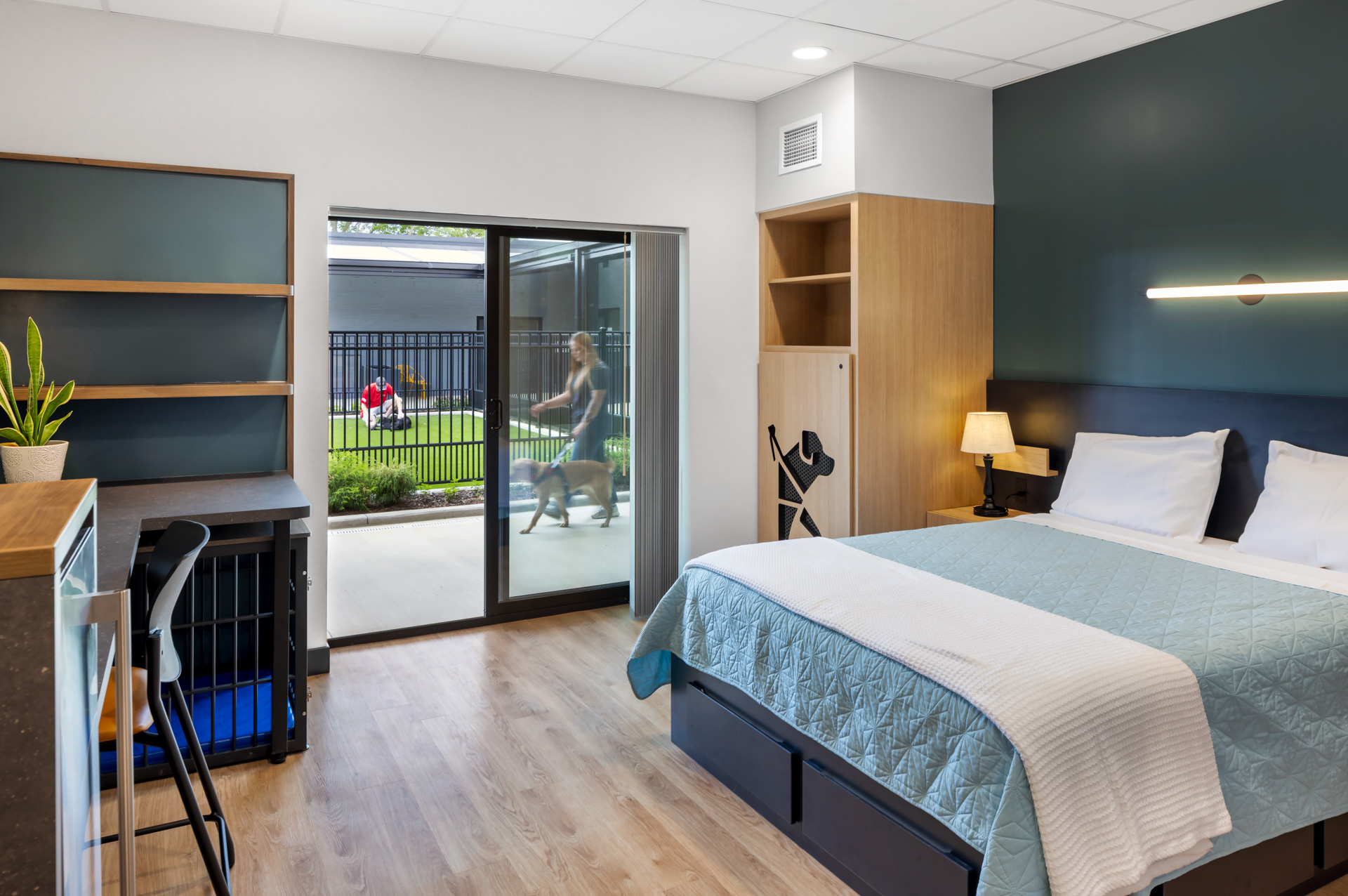 Student Residence bedroom at Pilot Dogs with a bed, desk, built-in dog crate, and sliding door to an outdoor courtyard