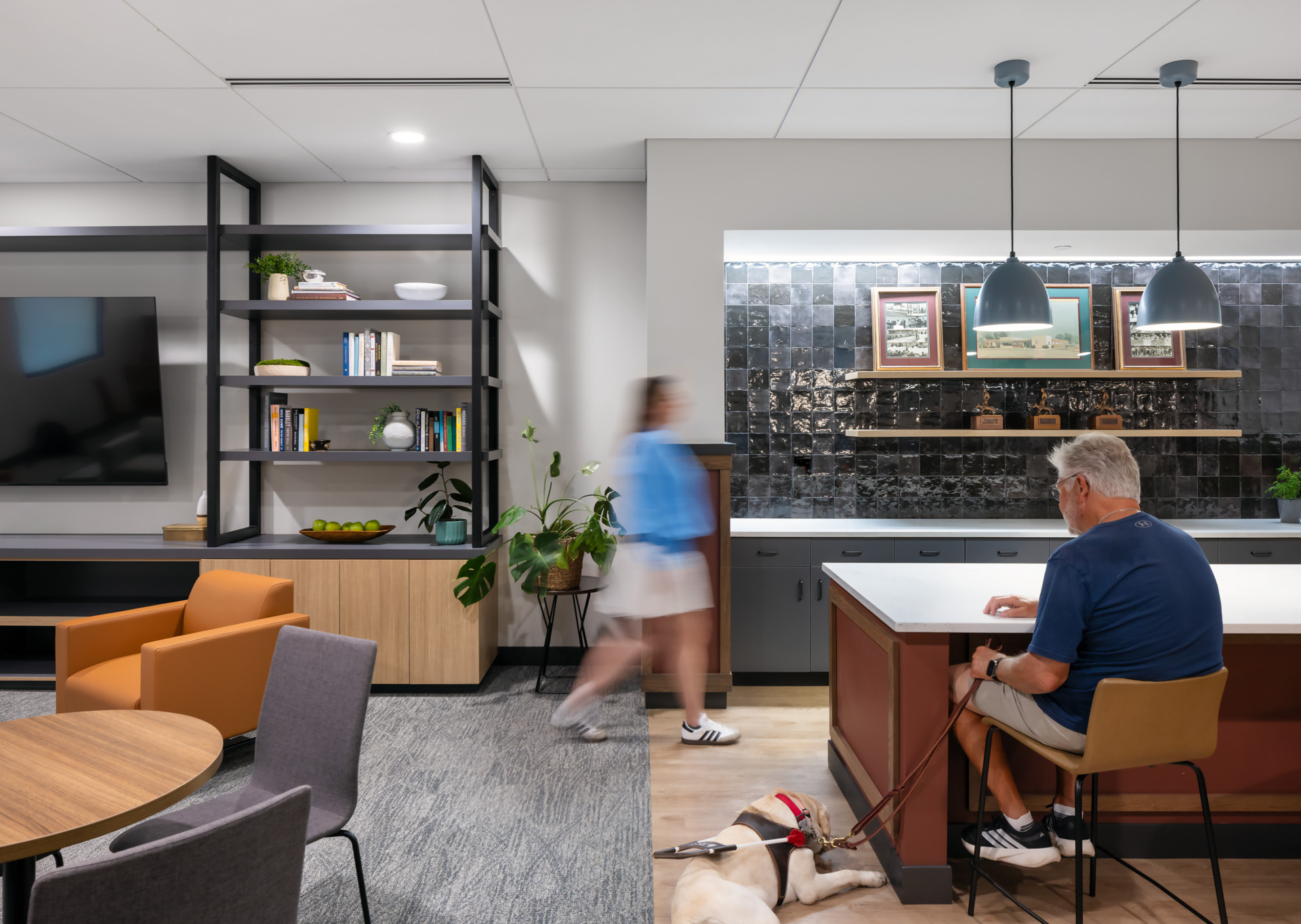Pilot Dogs recreation room with a kitchen island, lounge seating, and a student seated with a guide dog