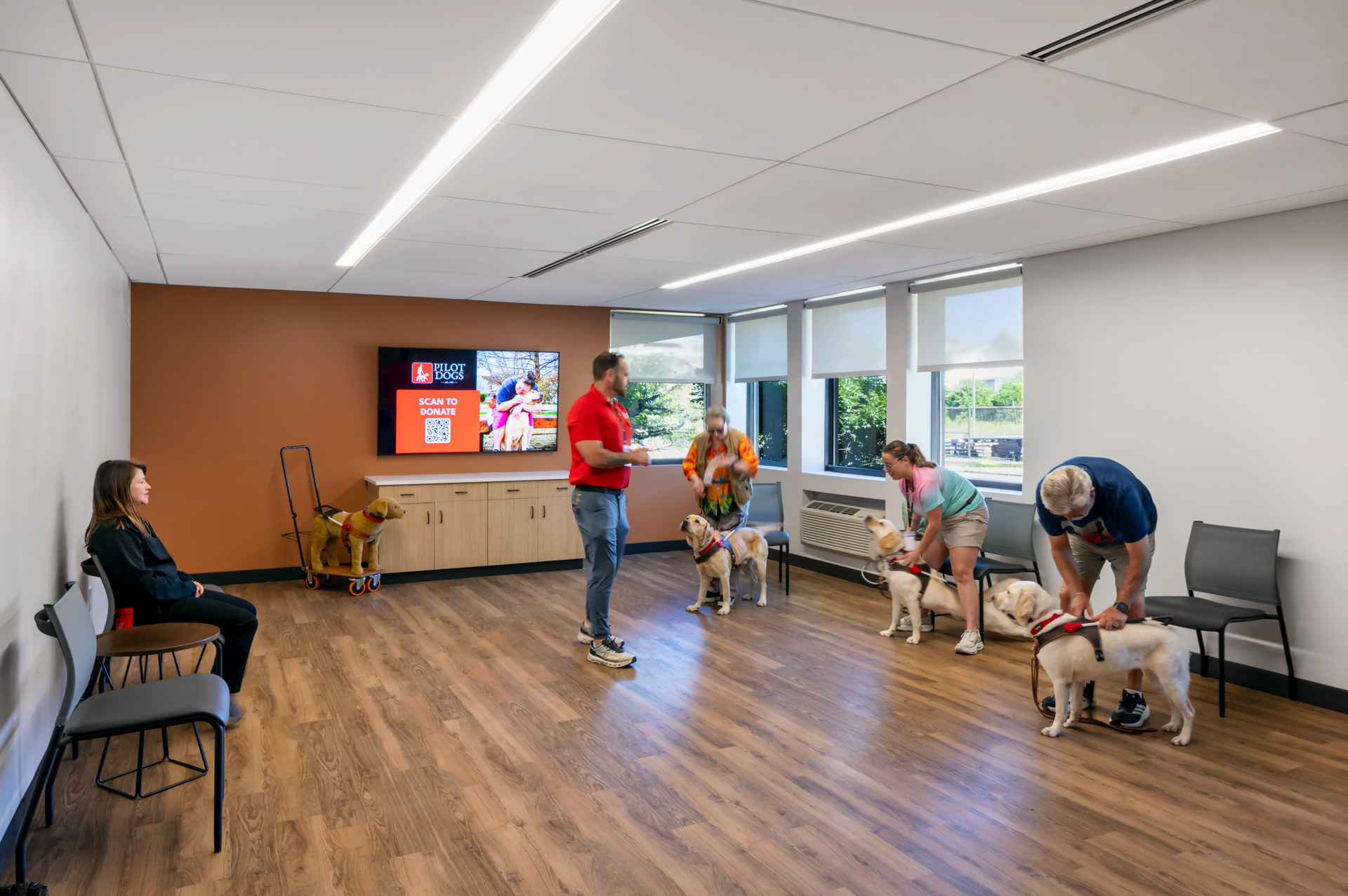 Pilot Dogs training room with students, instructors, and guide dogs practicing together in an open space