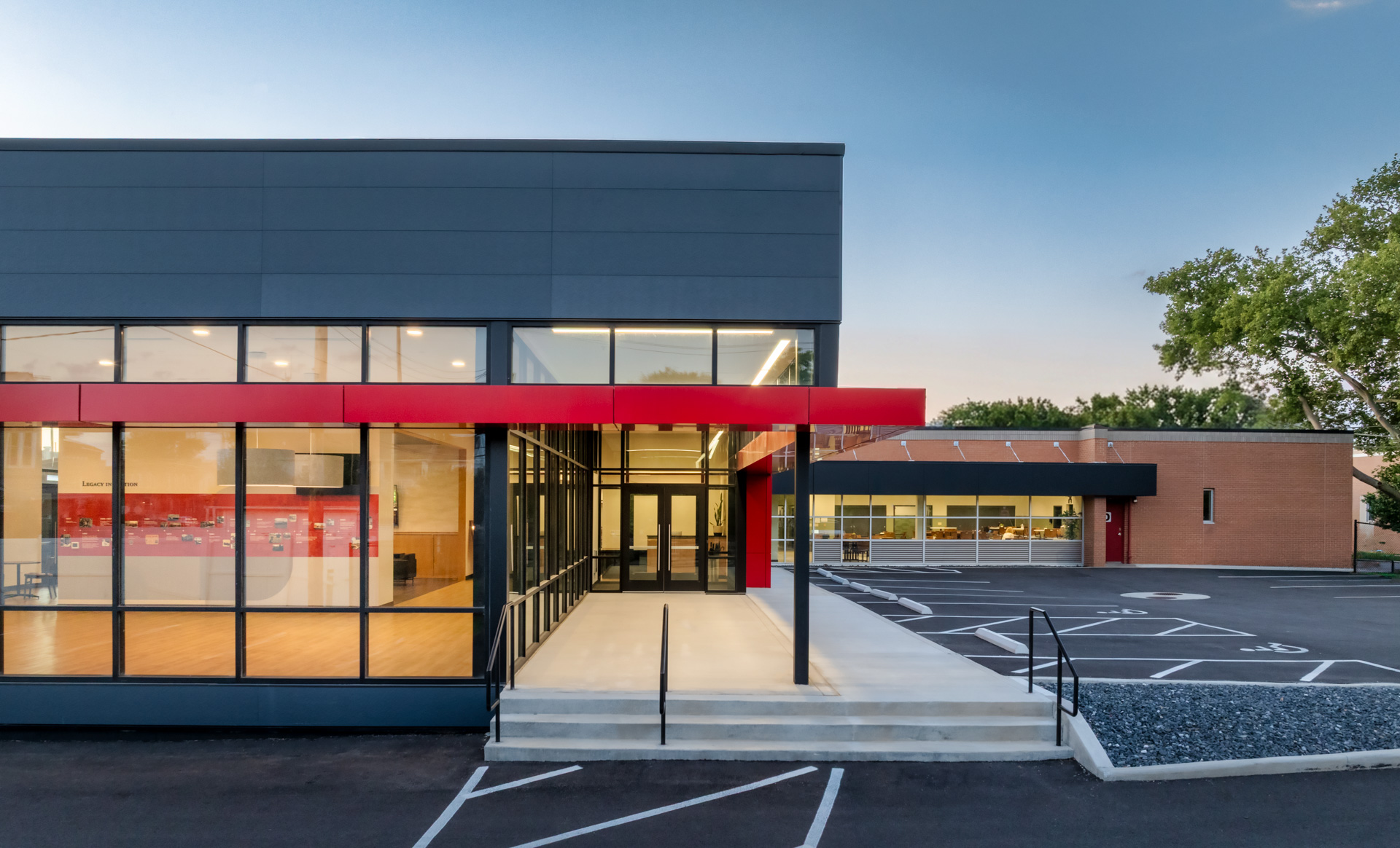 Exterior entrance of the Pilot Dogs Student Residence with large windows, a red canopy, steps, and view of existing brick building