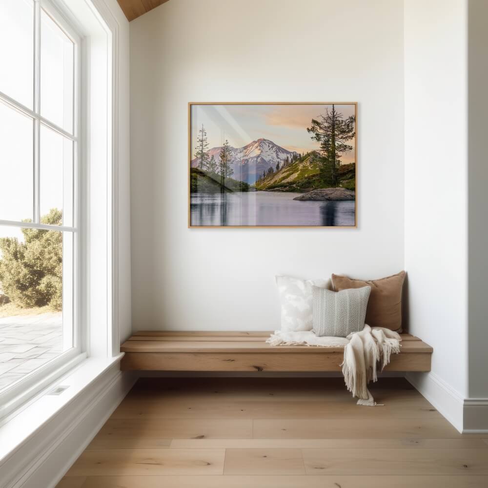 A photo print of Mount Shasta at sunset hangs on a wall in a modern minimalist entryway with light coming in and reflecting on the frame from the left.