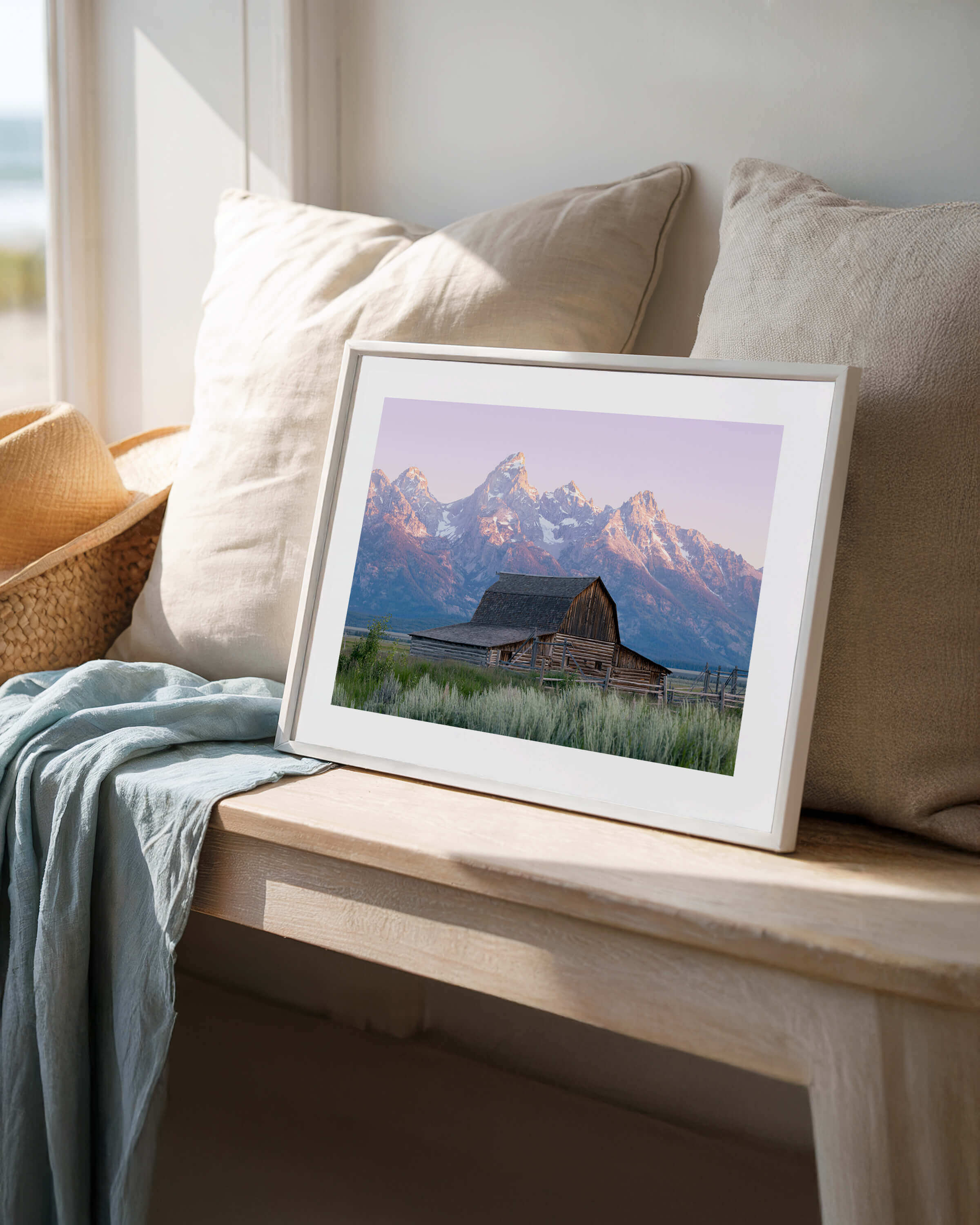 A framed photo of a barn in Grand Teton National Park resting on a bench with pillows