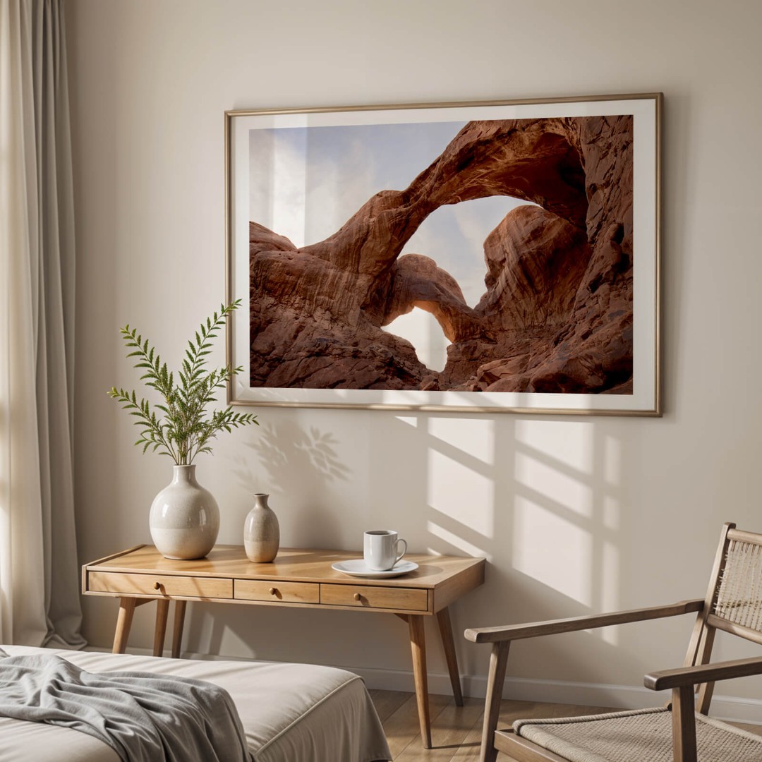 A framed photo of Double Arch in Arches National Park hanging on a wall above a table in a bedroom