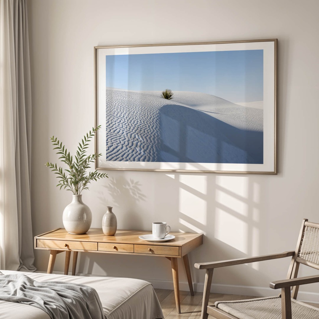 A framed photo of a single yucca plant in White Sands National Park hanging on a wall in a bedroom above a table