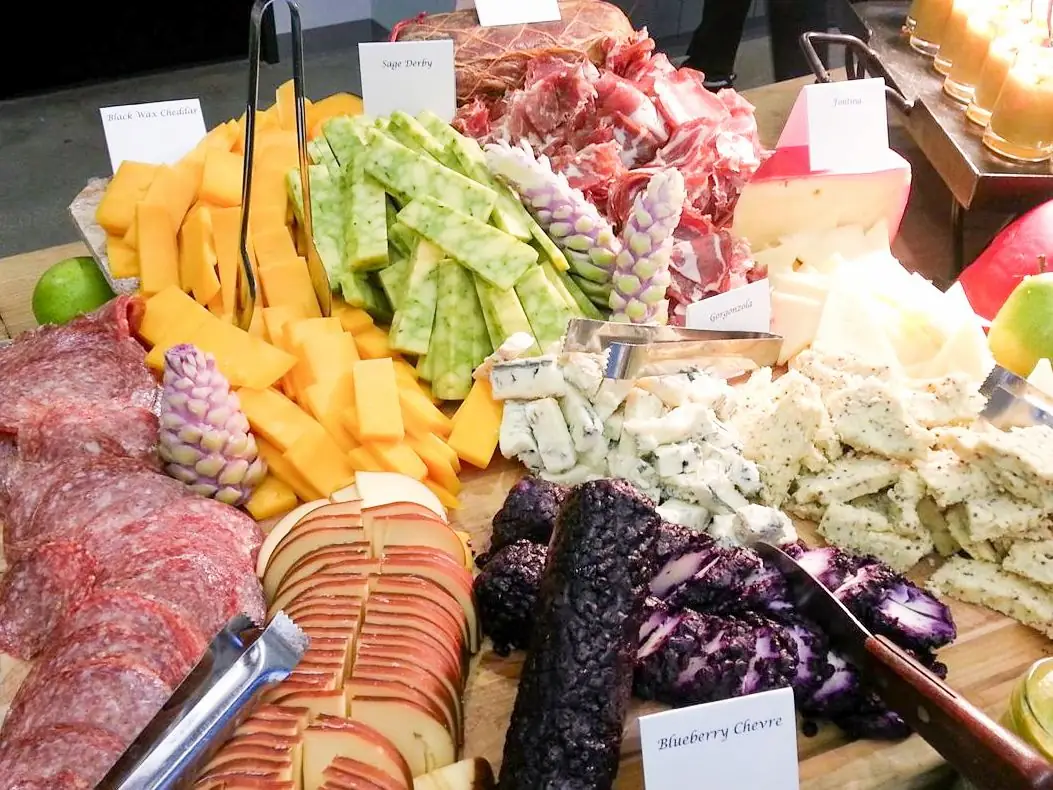 Assorted cheese and charcuterie board featuring labeled cheeses sliced meats and decorative edible flowers.