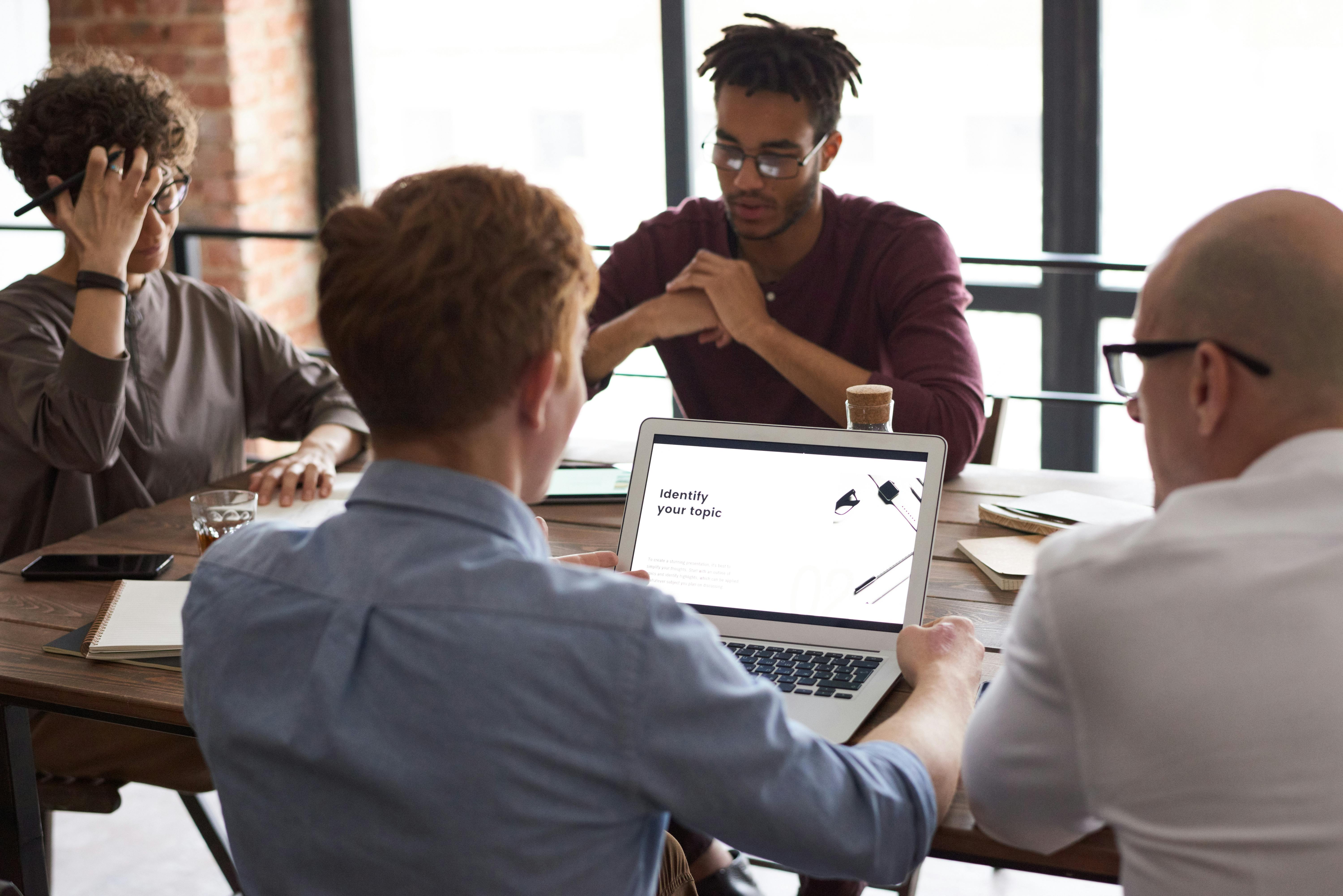 Team of diverse professionals collaborating in a modern office meeting, reviewing a presentation on a laptop during a strategic planning session.