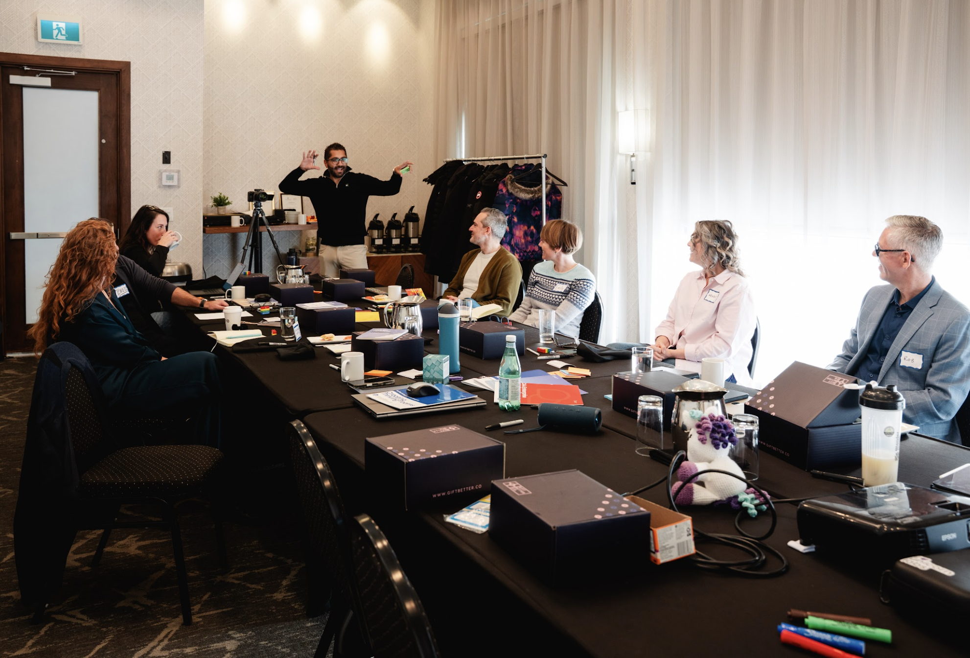 Board room meeting with people around a long table listening to presenter.