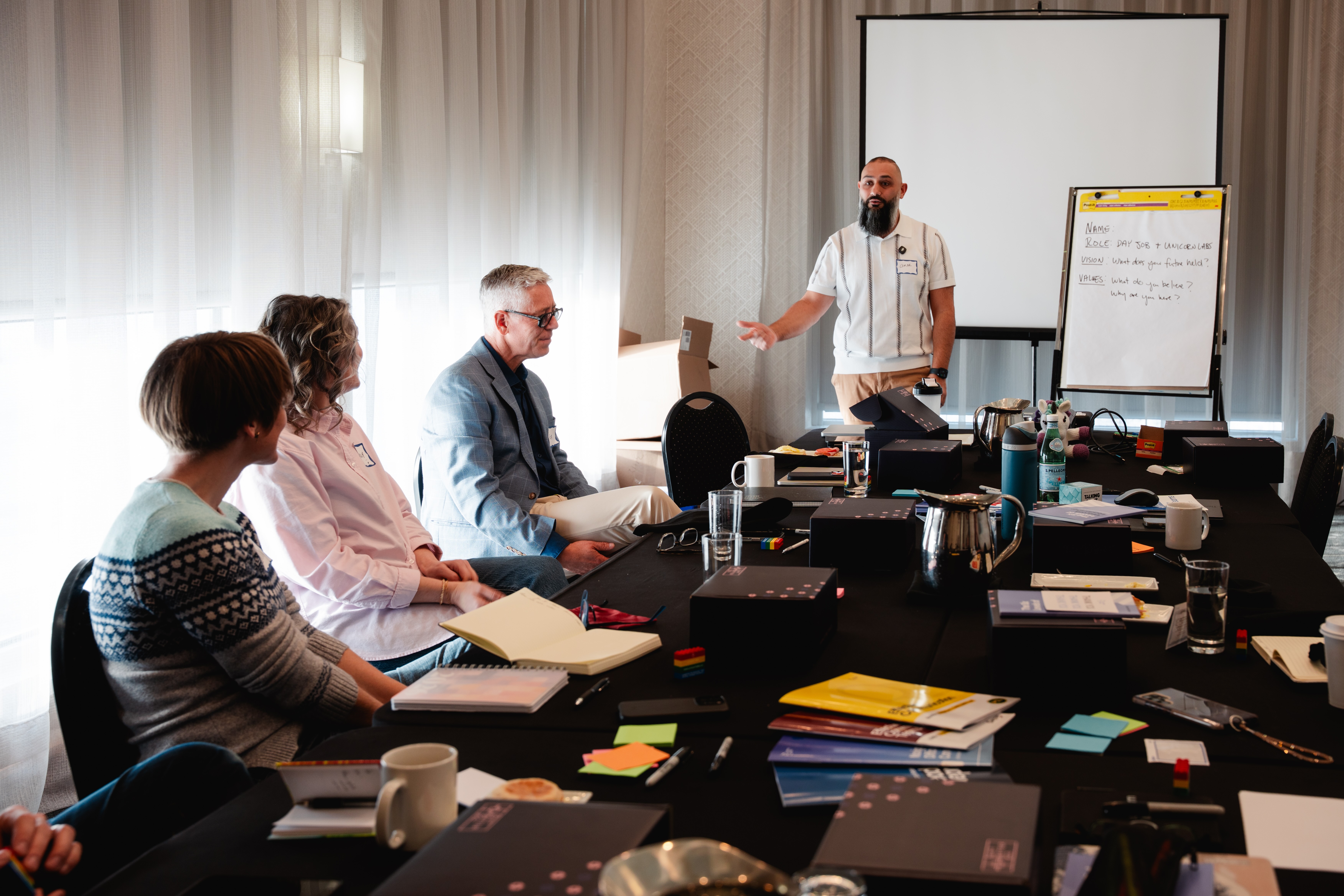 Unicorn Labs facilitator presenting to a small group of executives at a leadership workshop, with a flip chart outlining vision and values questions in the background