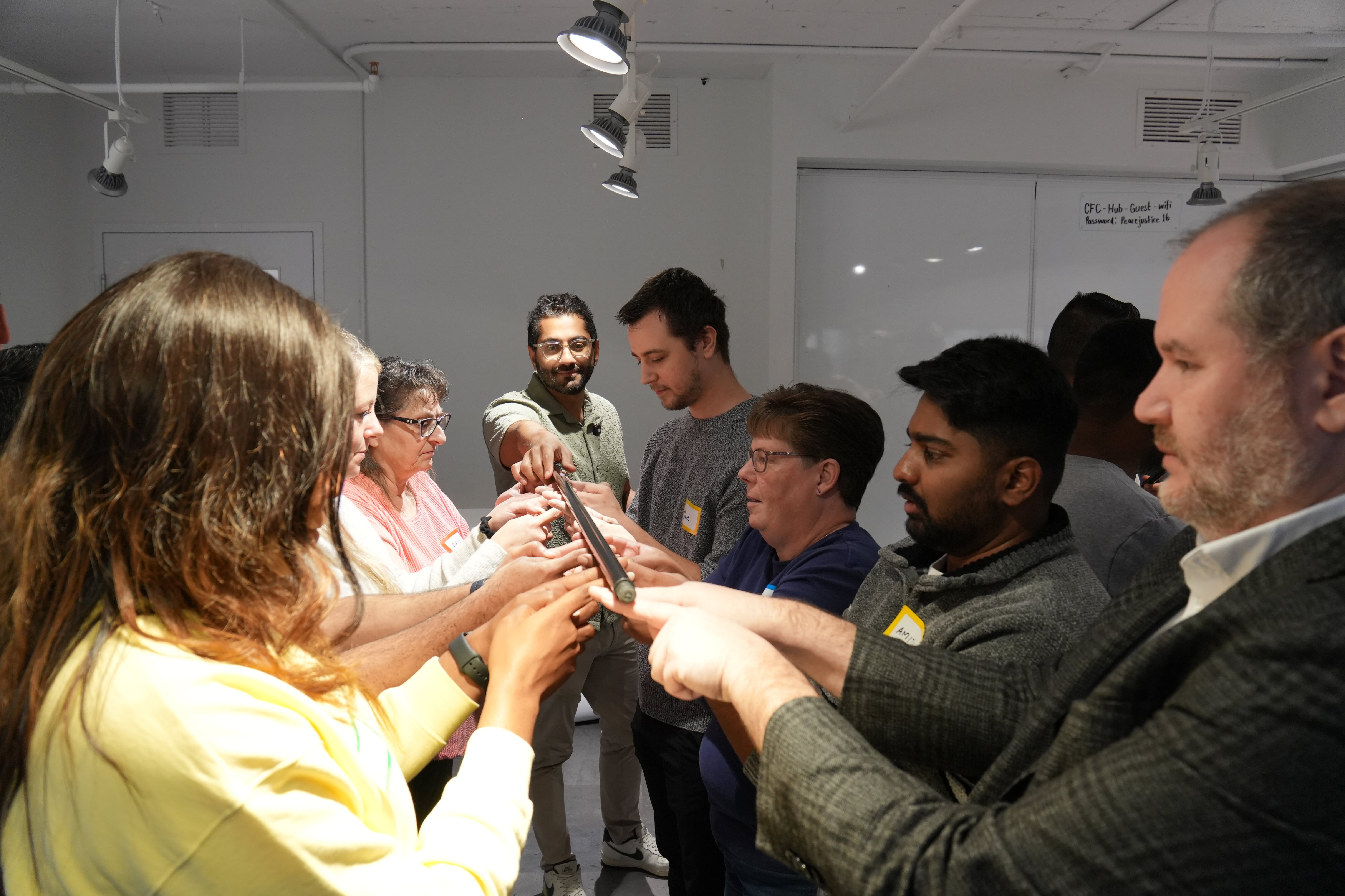 A diverse group of leaders standing in a circle, balancing a thin pole on their fingertips during a Unicorn Labs team-building exercise