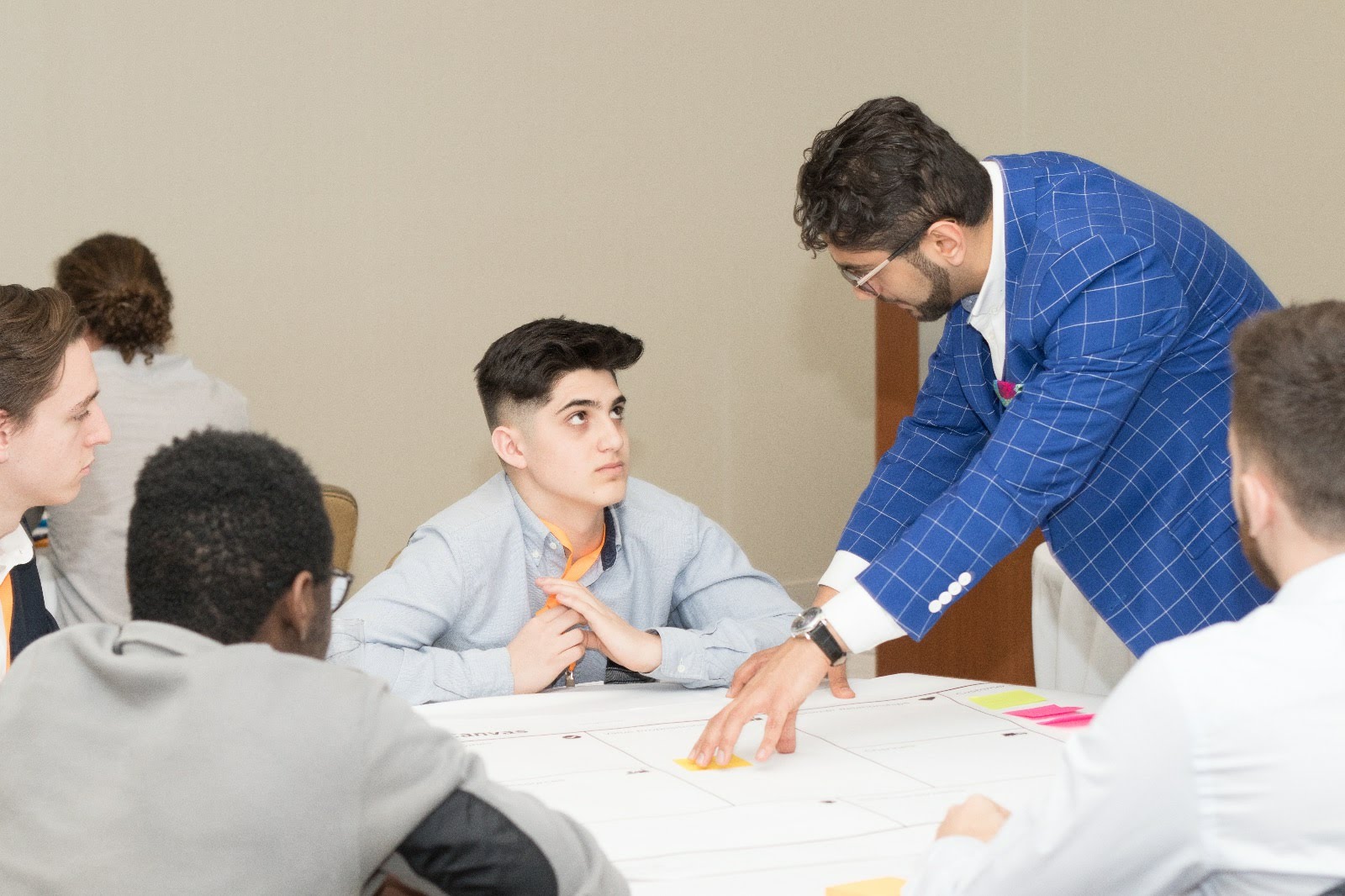 Fahd Alhattab coaching a young participant through a canvas worksheet exercise at a leadership workshop table, pointing to a sticky note while the group works