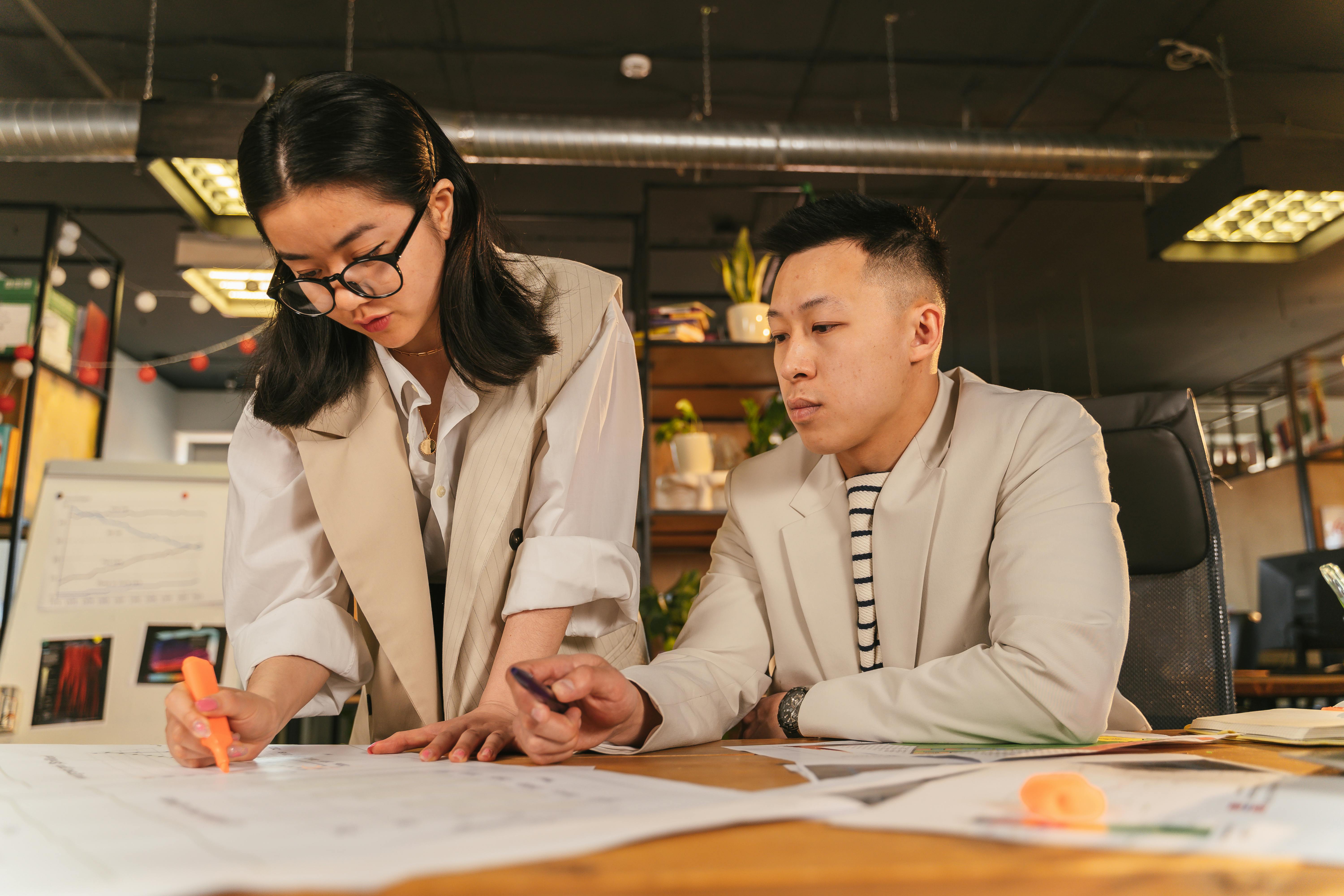 Two colleagues reviewing strategy documents and charts together at a desk in a modern office, a manager coaching a team member through planning work