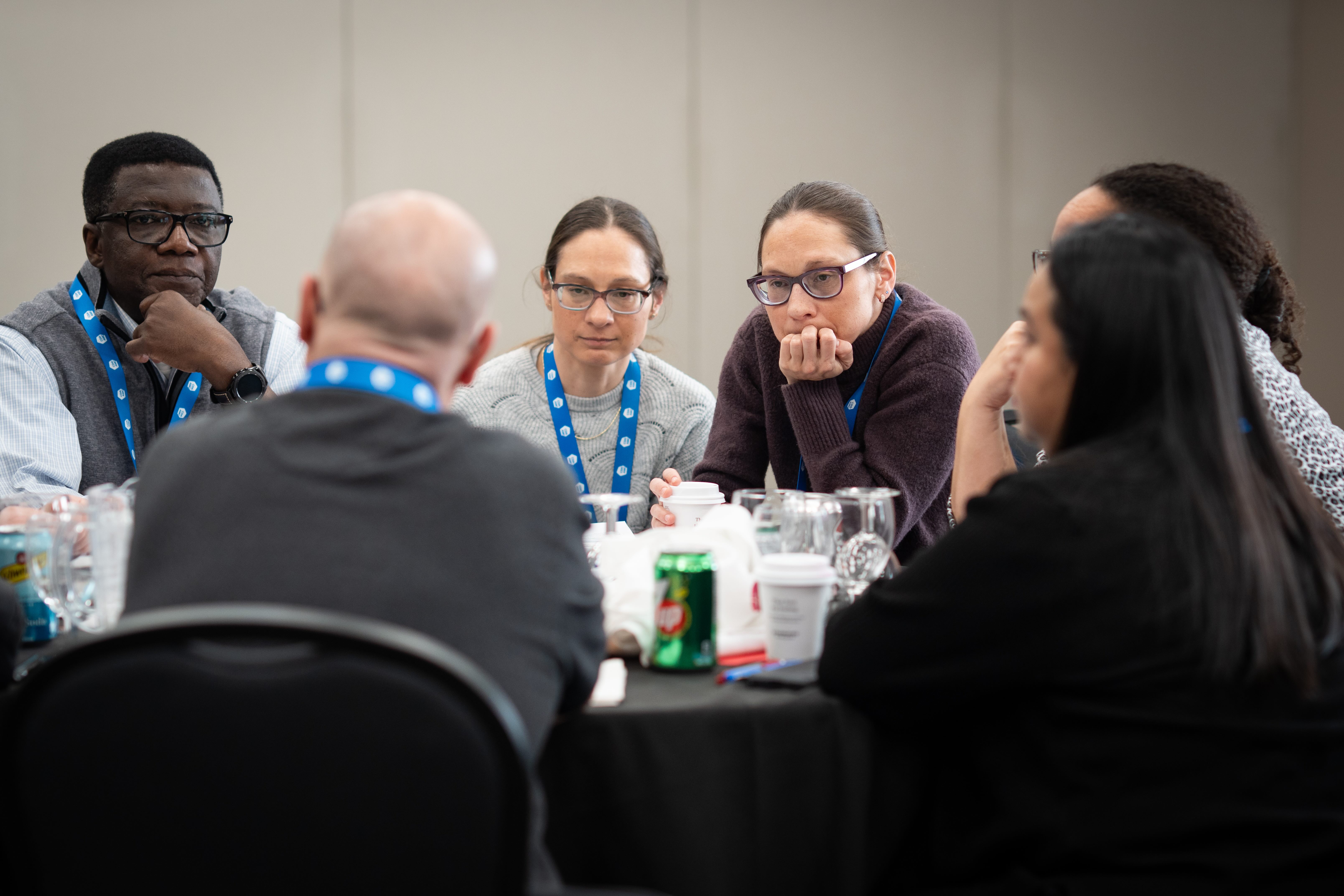 Small group of leaders listening intently during a discussion at a round table, wearing conference lanyards at a leadership workshop