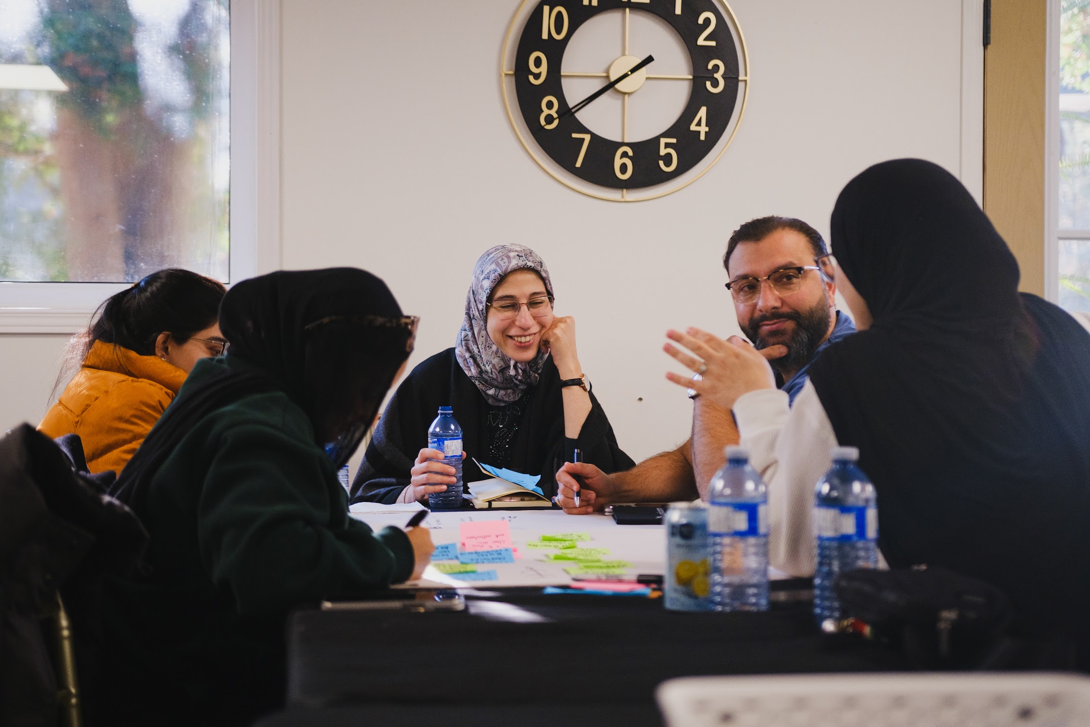 Small group of workshop participants smiling and discussing ideas around a table with colourful sticky notes during a leadership breakout exercise