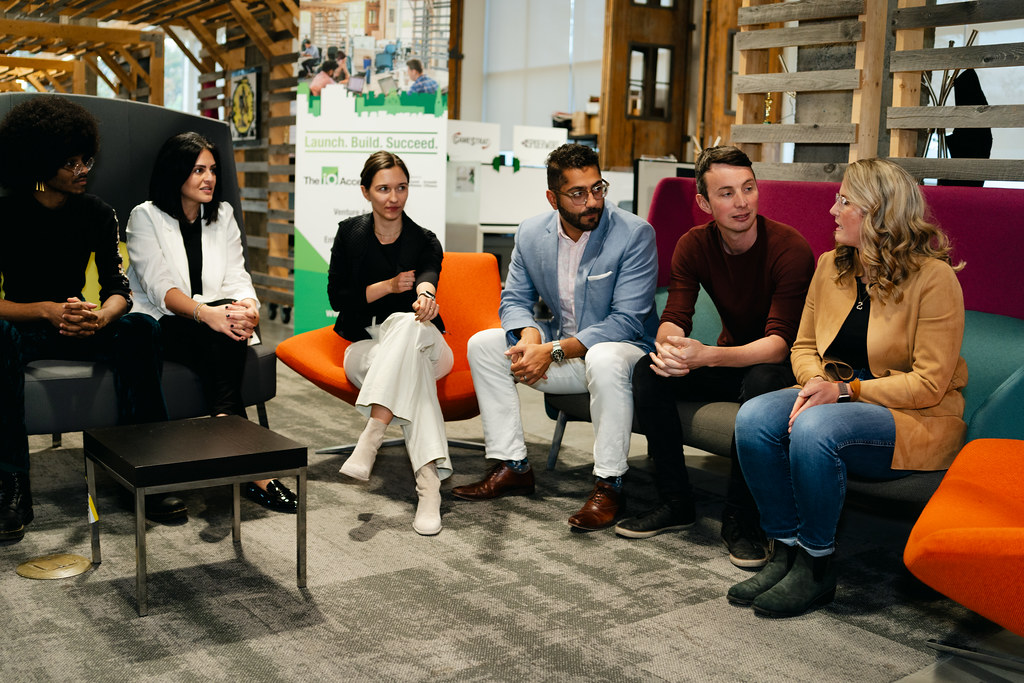 Small group of professionals seated on lounge chairs in an open workspace, having a relaxed team discussion during a workshop or networking session