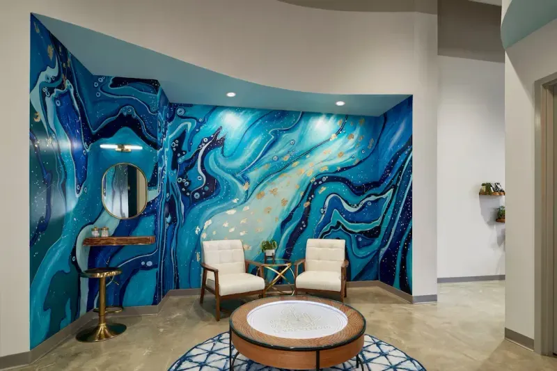 Recovery lounge at sēk Sauna Studio with the blue geode mural, white chairs and a round kinetic sand table