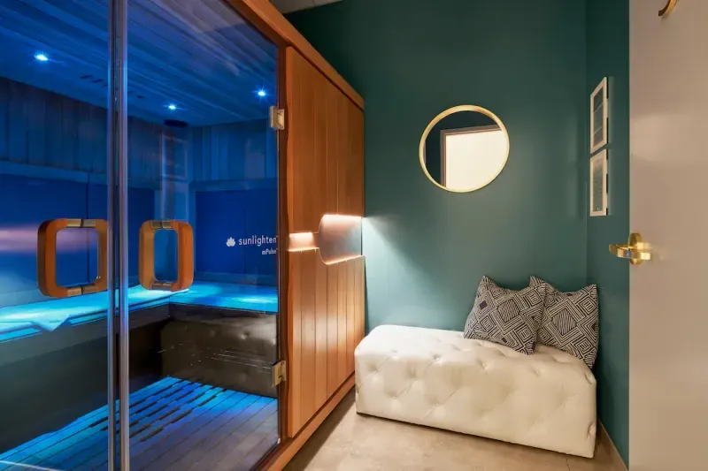 Full-size infrared sauna cabin at sēk Sauna Studio with a glass front, wood interior and blue chromotherapy light