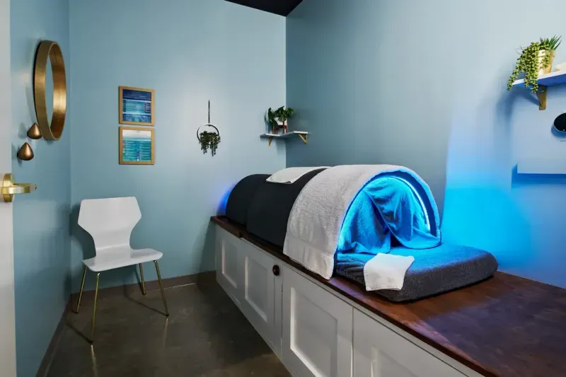 Private infrared sauna pod room at sēk Sauna Studio with the pod lit blue and folded towels on the bench