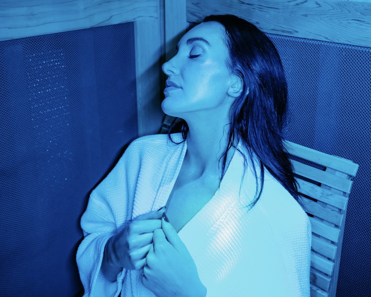 Guest relaxing in blue chromotherapy light on the bench of the infrared sauna cabin