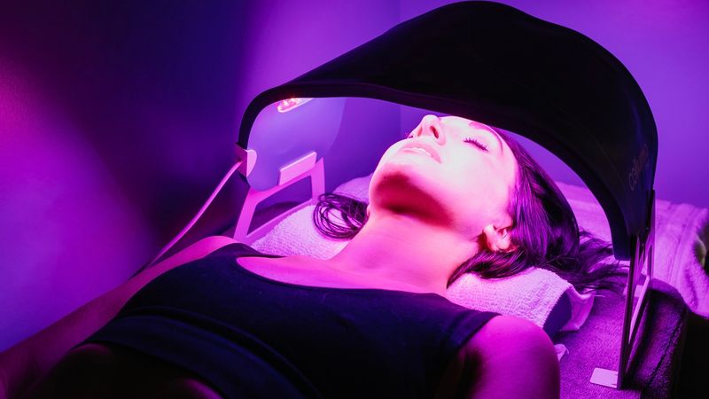 Guest under a Celluma red light therapy panel during a facial session at sēk Sauna Studio