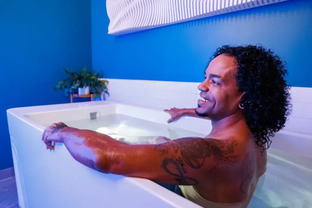 Guest smiling in the cold plunge tub in a private plunge room at sēk Sauna Studio.