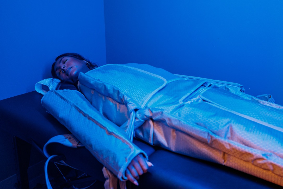 Guest resting in the full-body pressotherapy suit under blue light at sēk Sauna Studio in Franklin, Tennessee.
