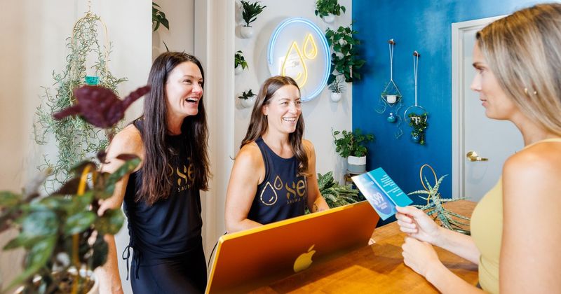 Two sēk Sauna Studio team members greeting a client at the front desk in Franklin, Tennessee