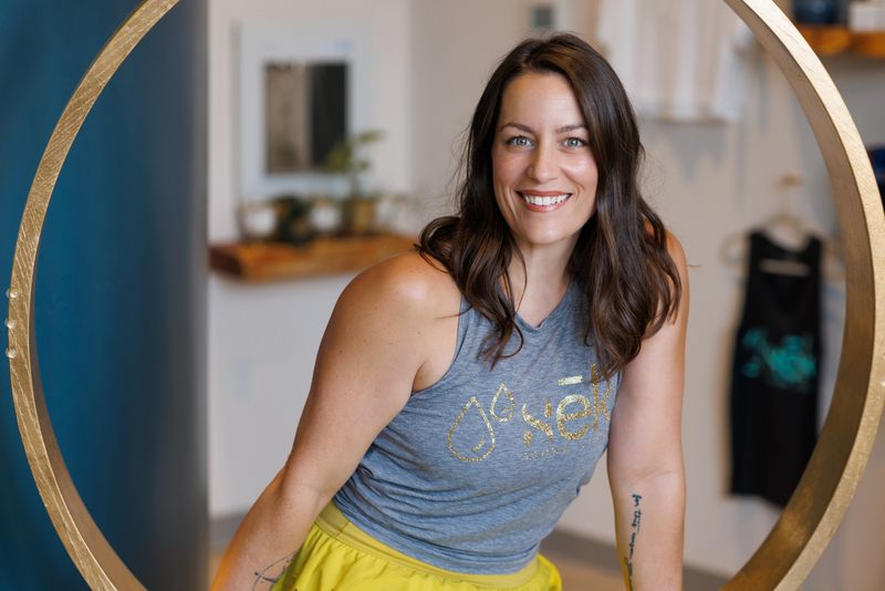 Lisa, studio manager at sēk Sauna Studio, sitting in the gold ring swing in the studio lobby in Franklin, Tennessee