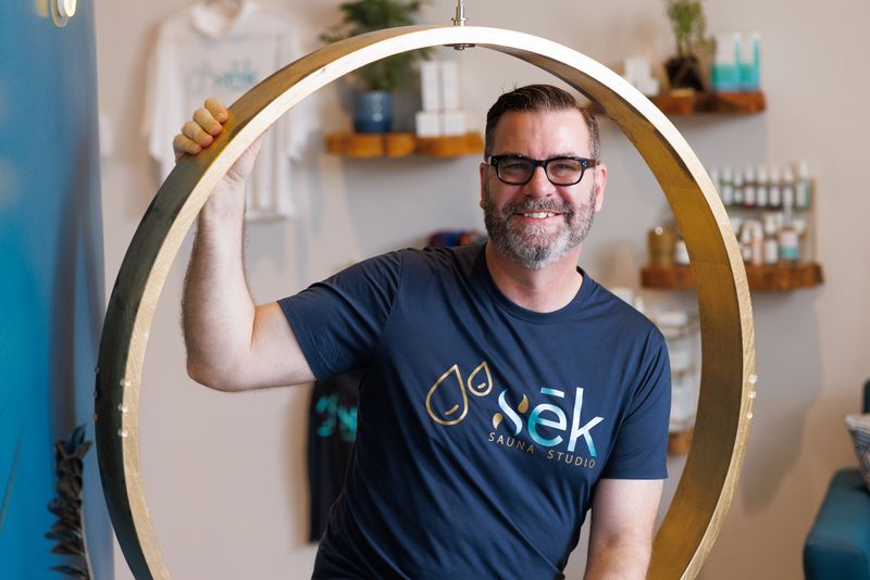 John Bryson, co-founder of sēk Sauna Studio, with one hand on the gold ring swing in the studio lobby in Franklin, Tennessee