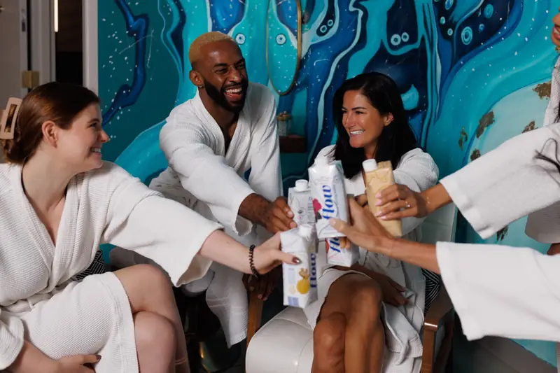 Party guests in robes toasting with Flow alkaline spring water at sēk Sauna Studio