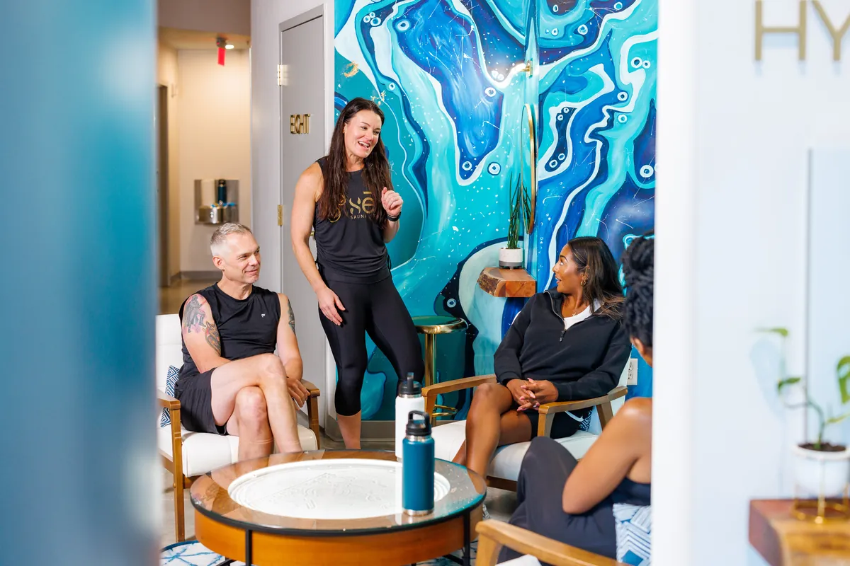Guests relaxing in the sēk lounge beside the blue mural with a team member