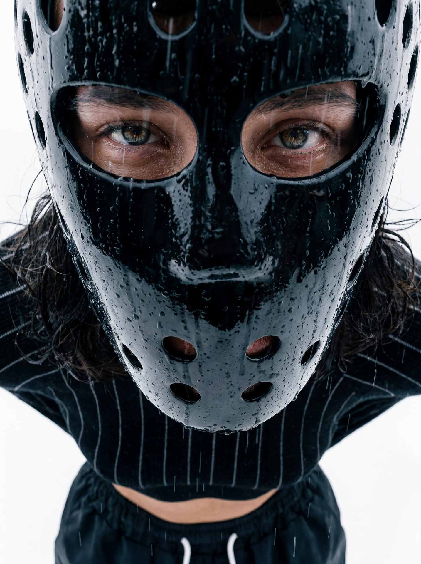 Person mit nasser schwarzer Maske mit Löchern, die direkt in die Kamera blickt.