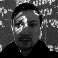 Junger Mann mit Lichtmustern auf Gesicht, umgeben von einer Wand mit geometrischen Formen.