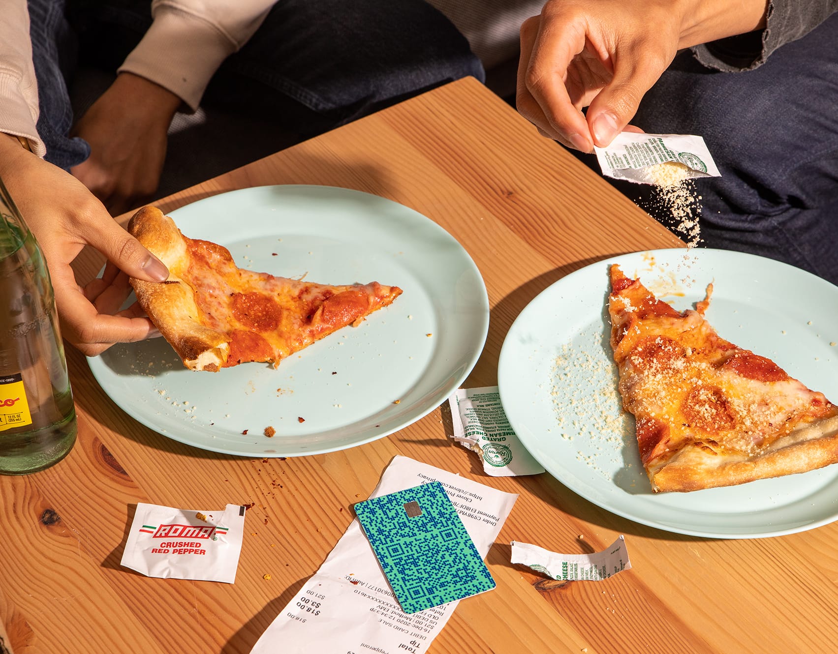 Two pizza slices on plates being shared, with a teal Venmo card and receipt on the wooden table