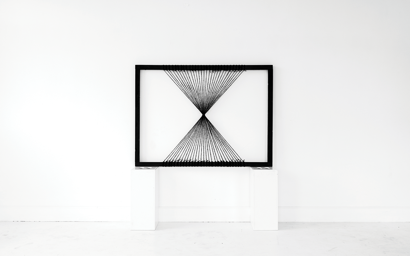 Large framed string art sculpture hung on a white gallery wall — geometric hourglass pattern of radiating black lines