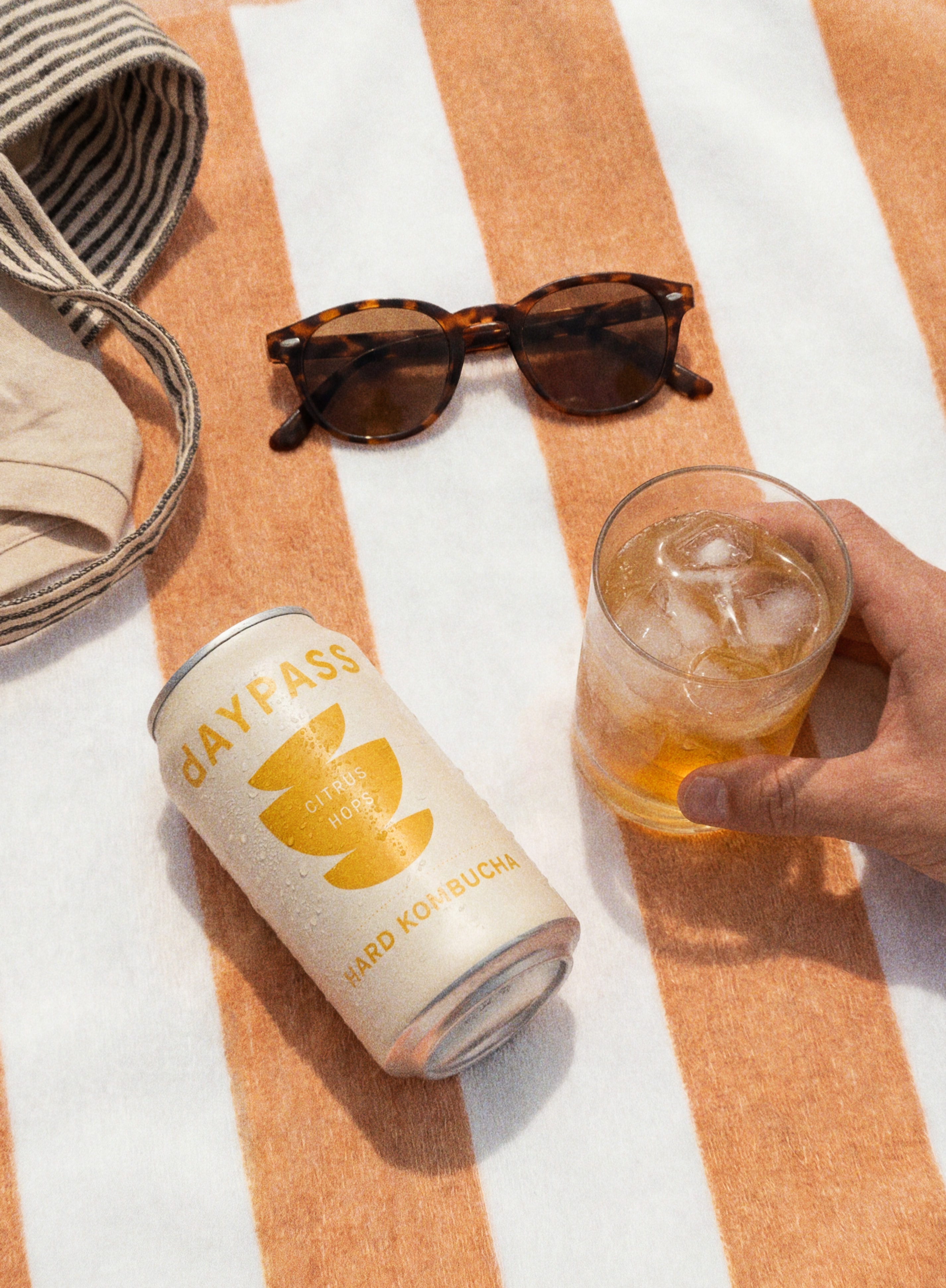 Daypass Citrus Hops can resting on a striped beach towel with sunglasses nearby