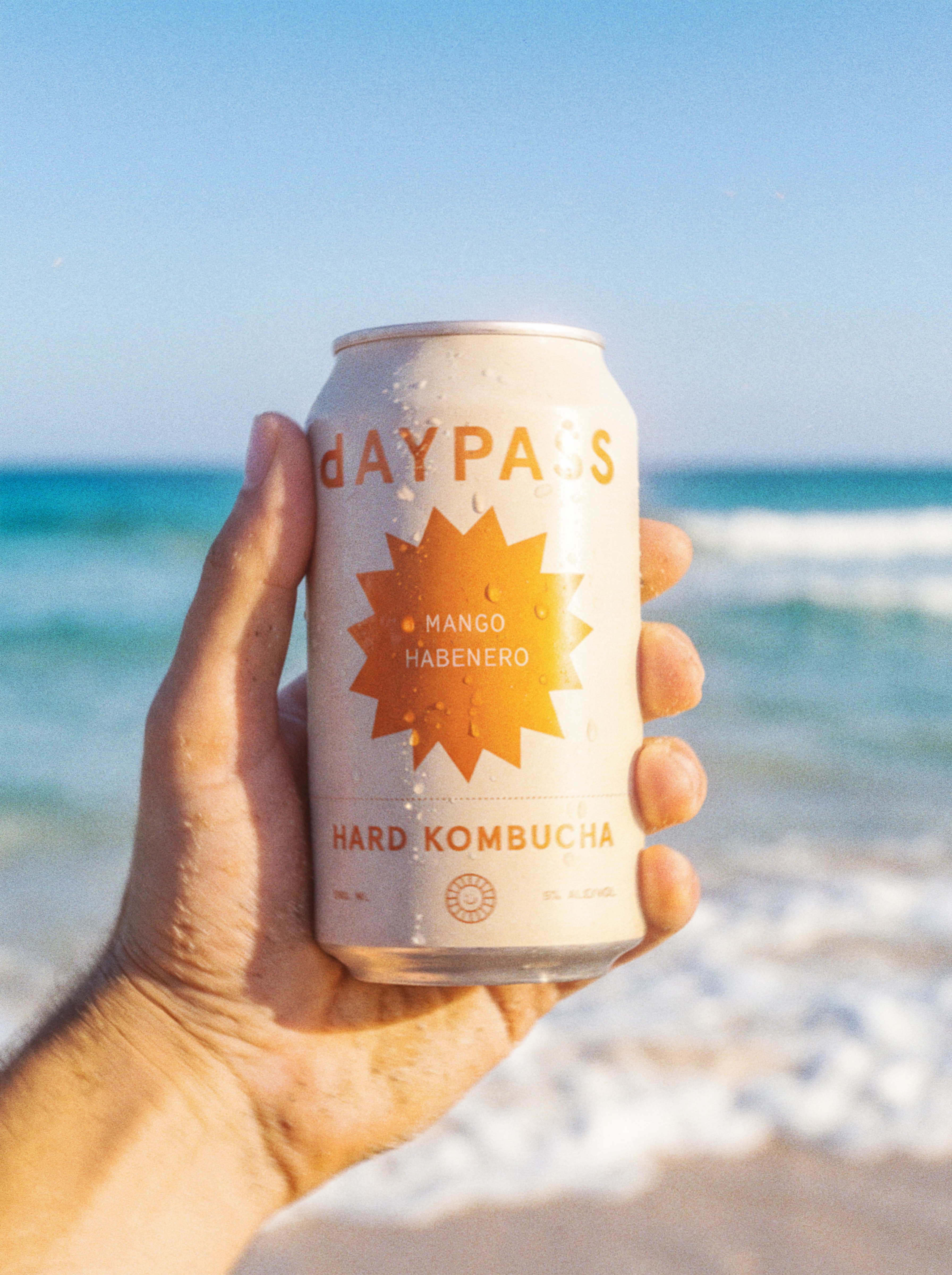 Hand holding a Daypass Mango Habanero can at the beach