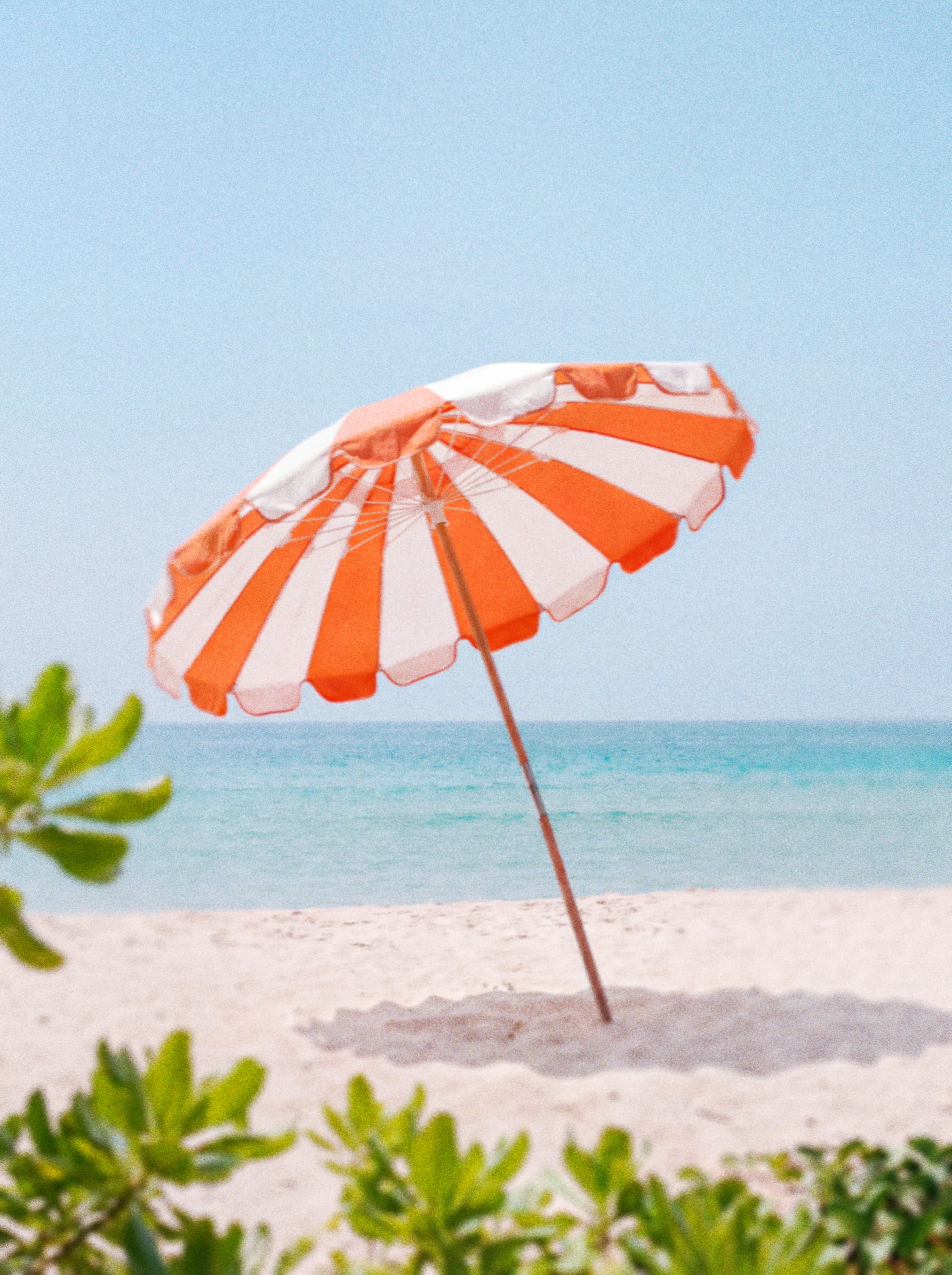 Person standing under an orange and white striped Daypass beach umbrella