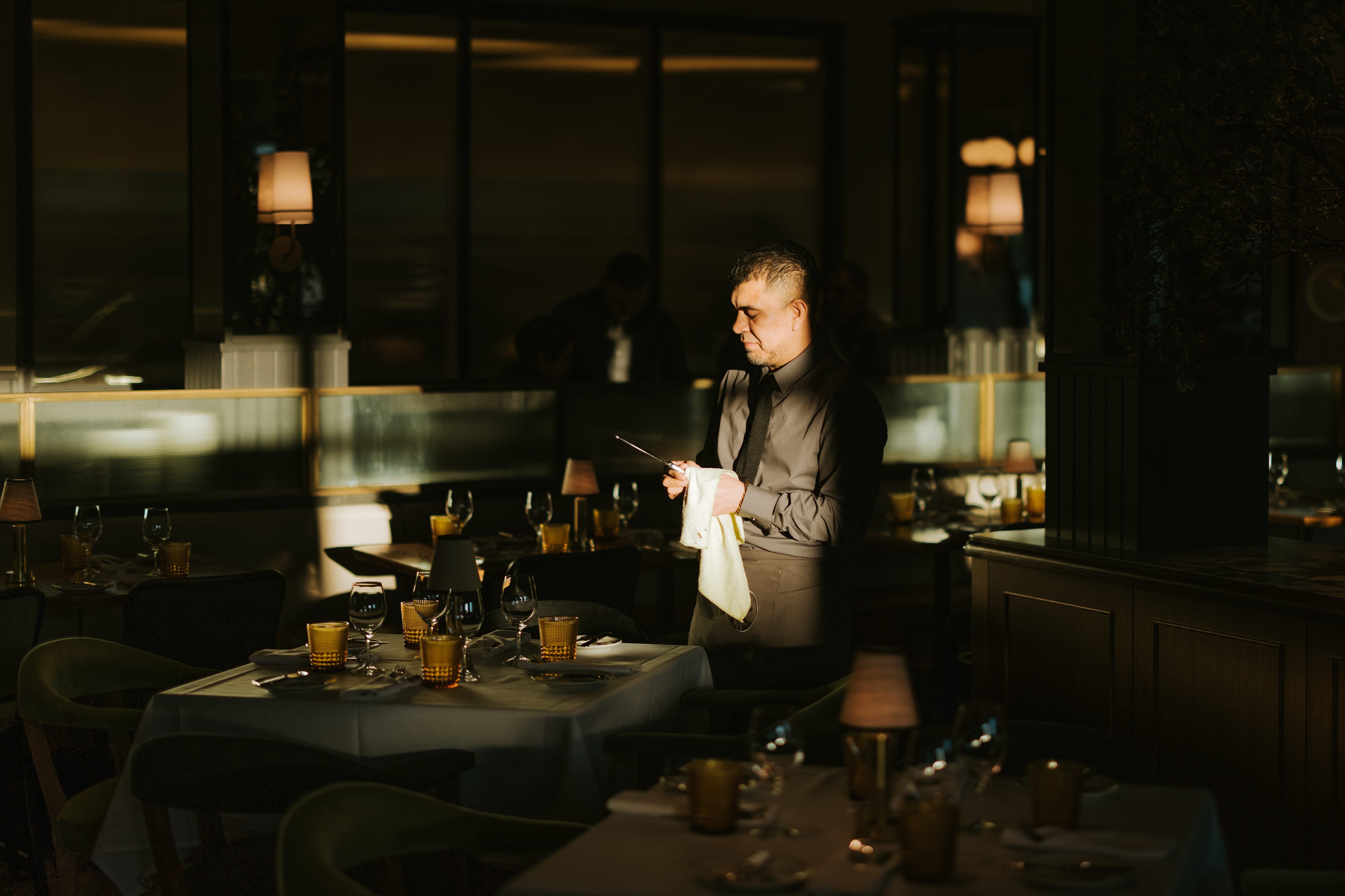 Waiter polishing cutlery in the moody candlelit dining room at Izzy's