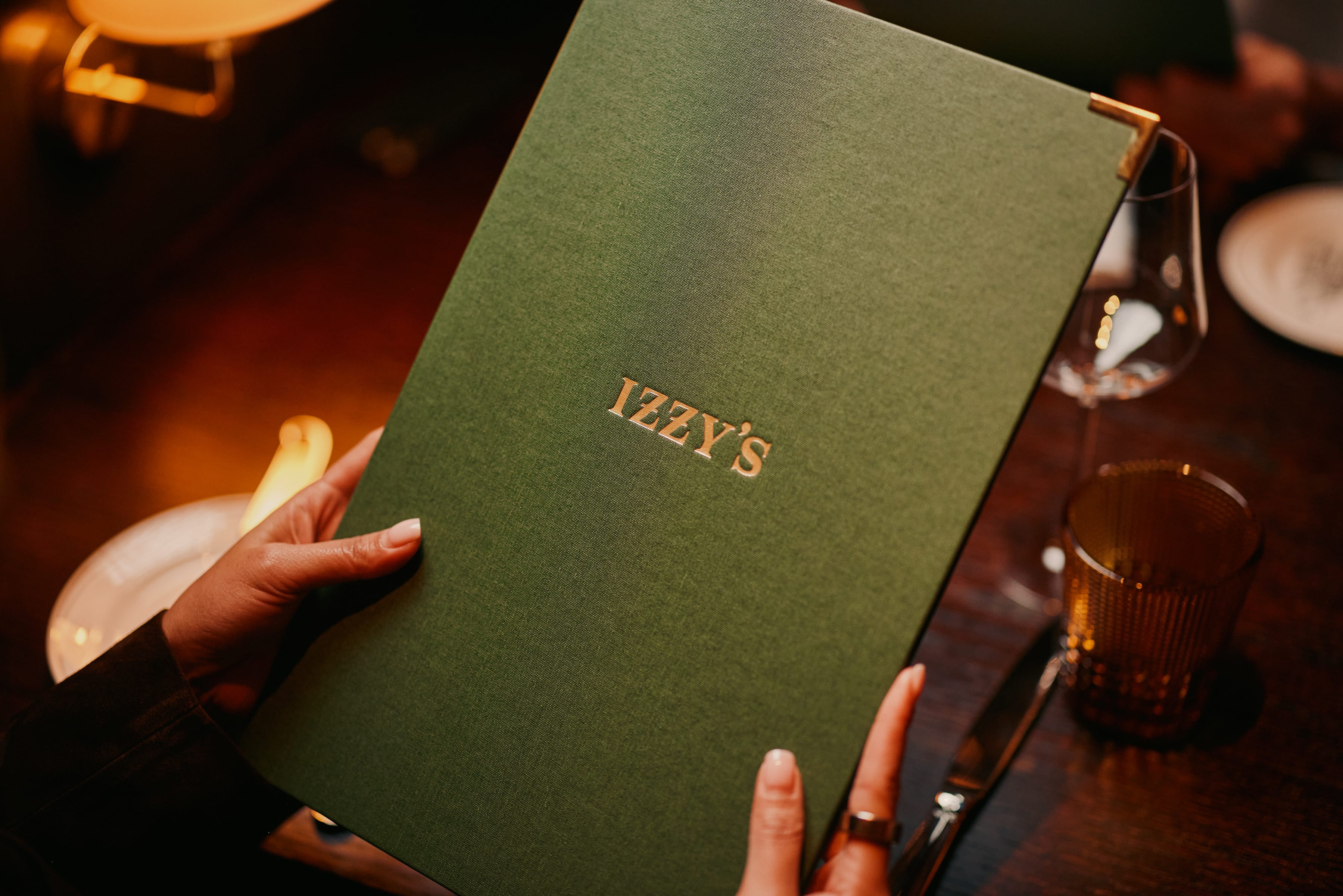 Hands holding the green Izzy's Steaks & Chops menu with gold embossed lettering
