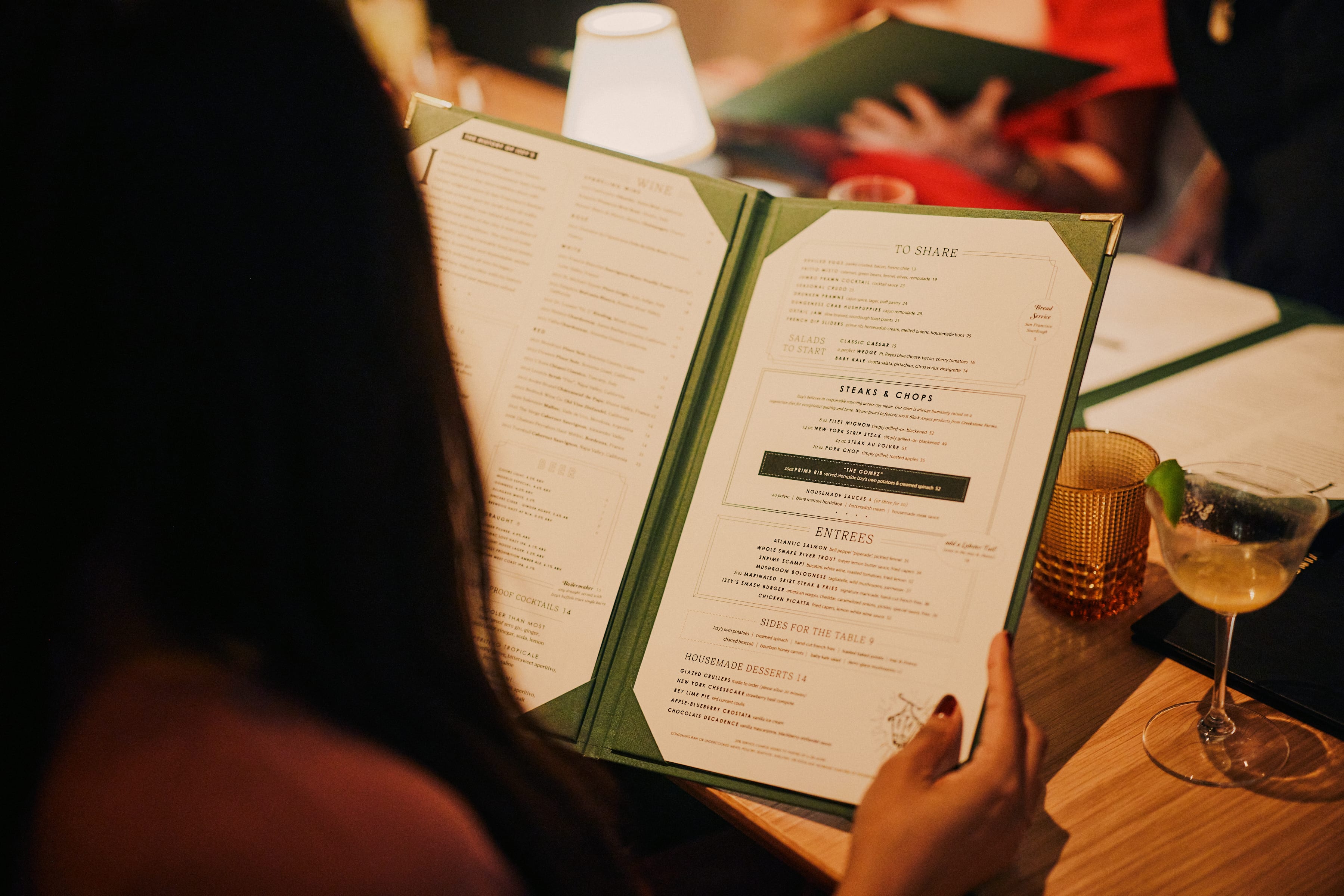 Diner holding open the green Izzy's Steaks & Chops menu with a cocktail on the table