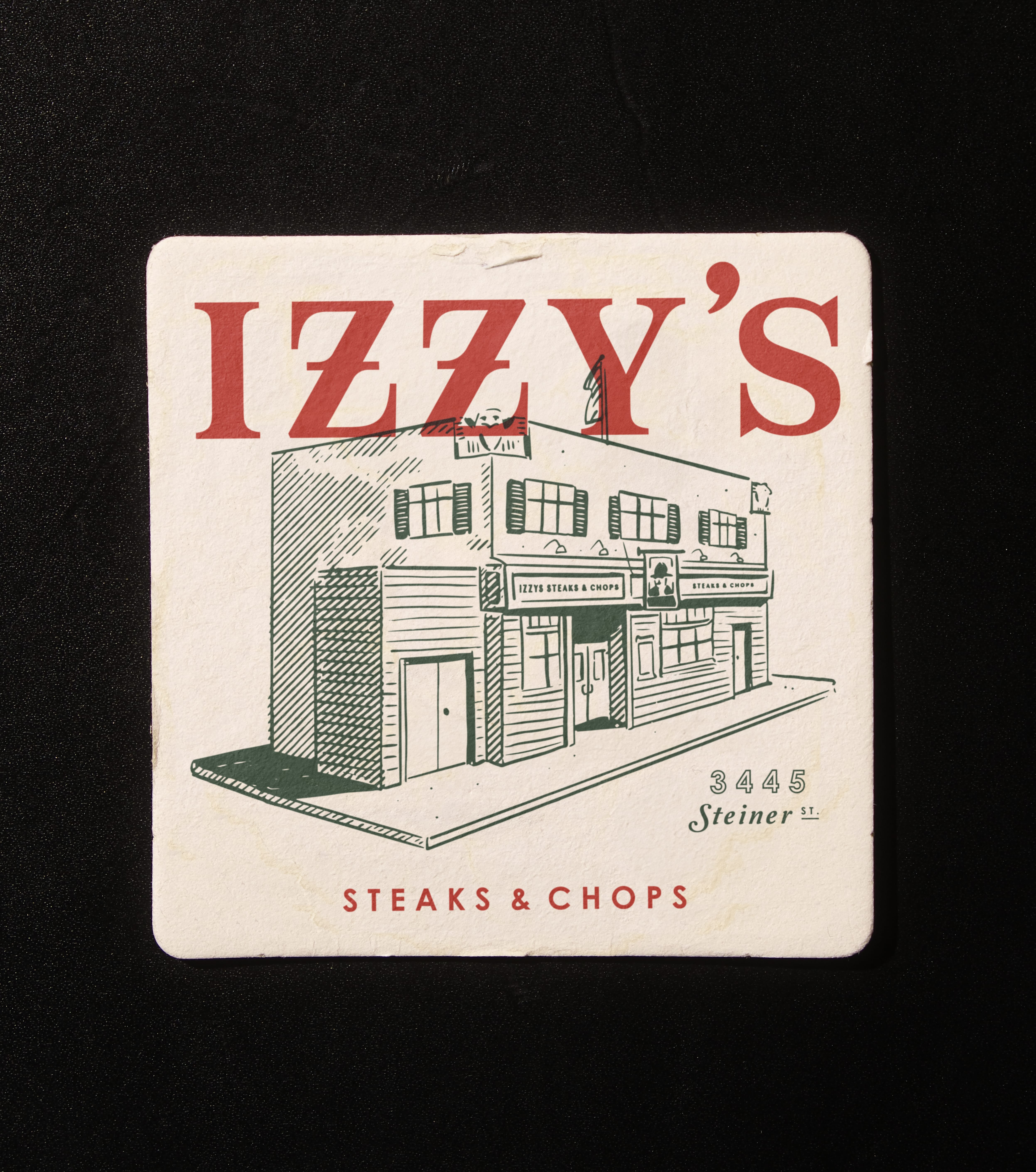 Square Izzy's Steaks & Chops coaster with building illustration and 'Steaks & Chops, 3445 Steiner St'