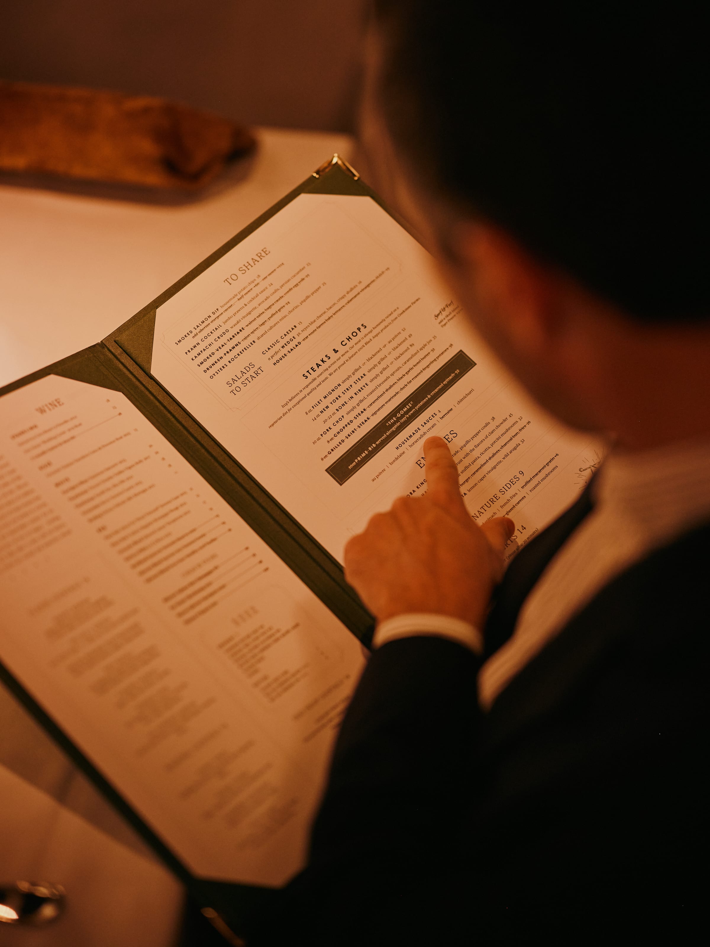 Guest reading and pointing at the Izzy's Steaks & Chops menu in a warm candlelit dining room