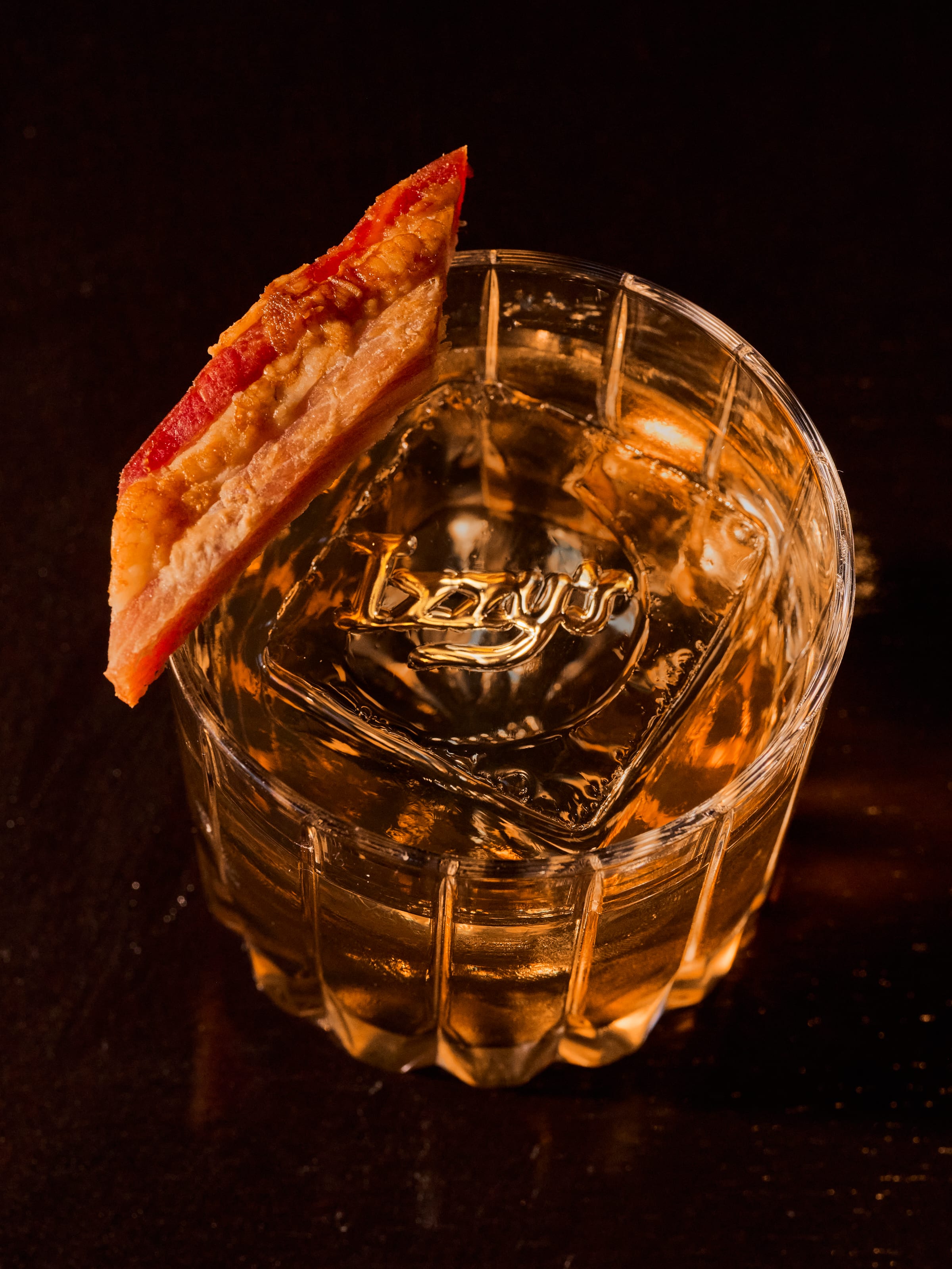 Overhead shot of an Izzy's branded rocks glass with a large ice cube, cocktail, and crispy garnish